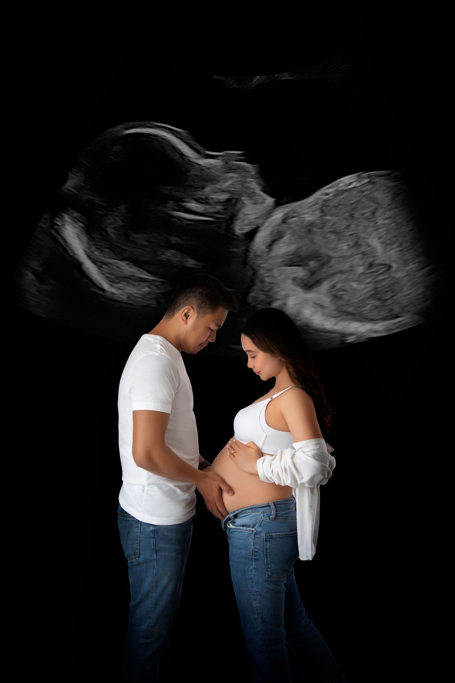 Black and white maternity photo of couple holding pregnant belly with ultrasound image backdrop.