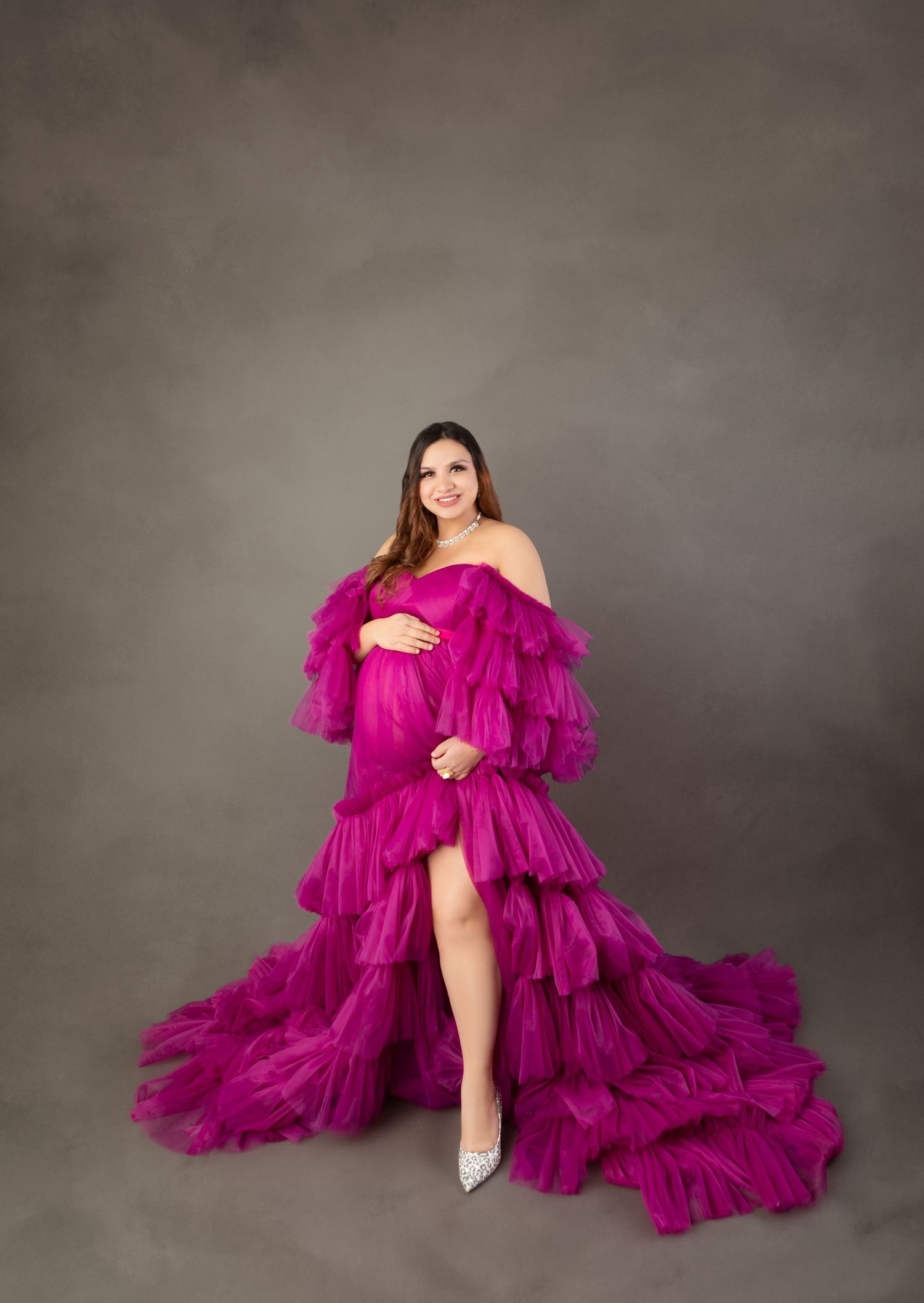 Pregnant woman in vibrant magenta ruffled tulle off-shoulder maternity gown in studio portrait.