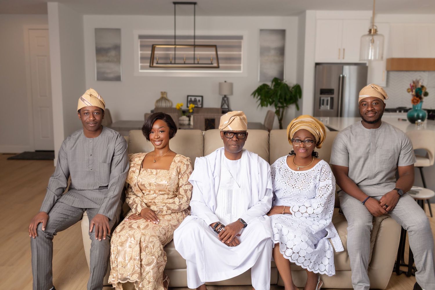 Five people in traditional Nigerian clothing seated and standing in modern living room.