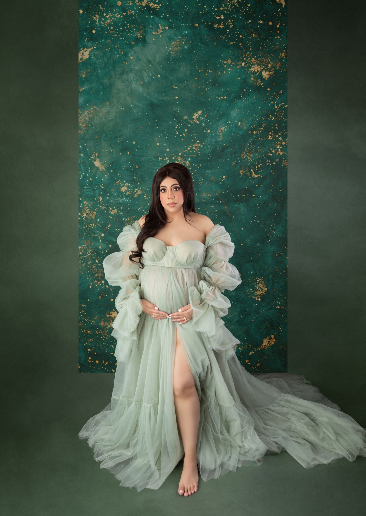 Pregnant woman in mint green ruffled maternity gown against teal and gold backdrop.