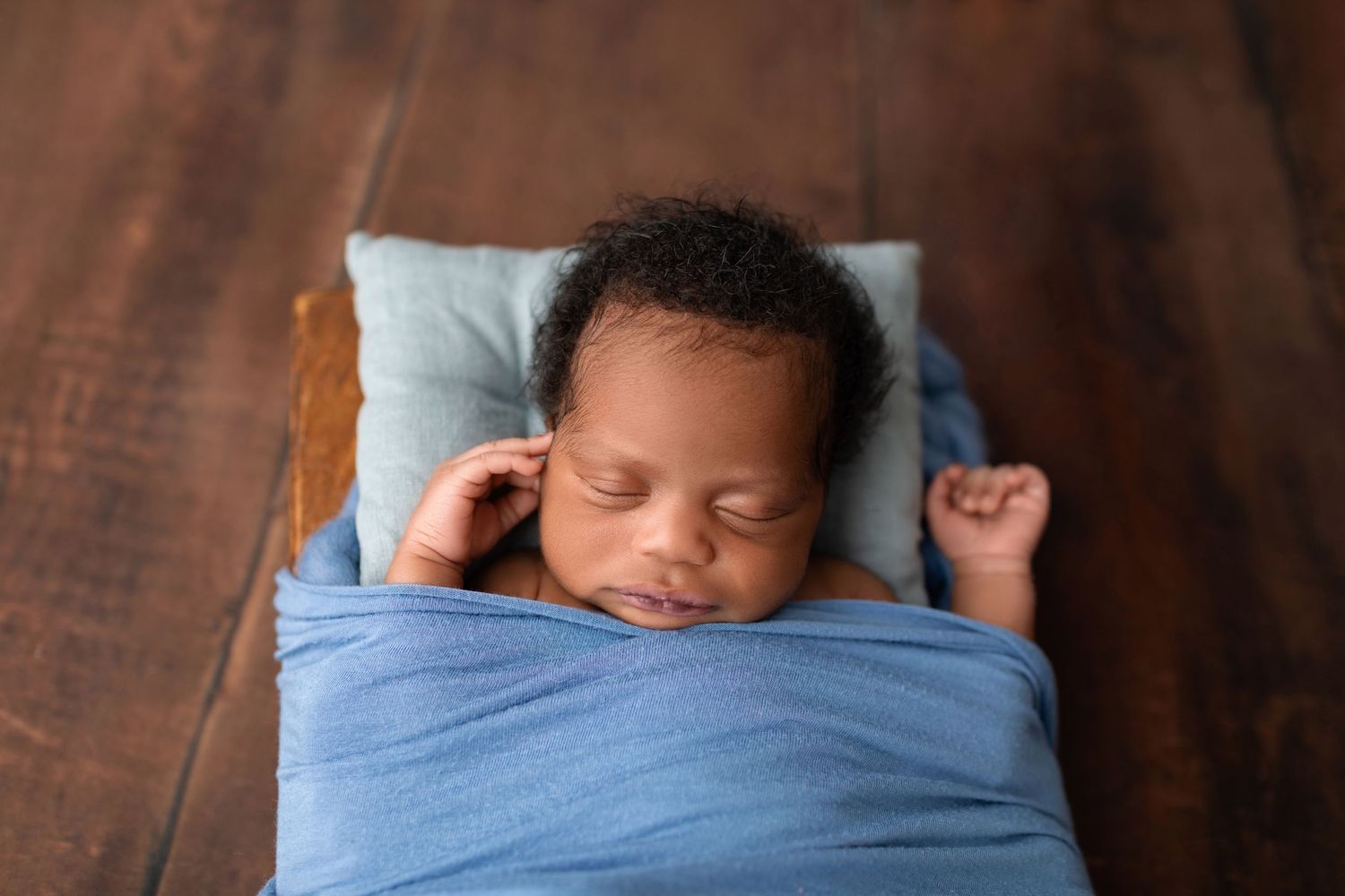 Peaceful newborn wrapped in blue sleeping in a tiny wooden bed.