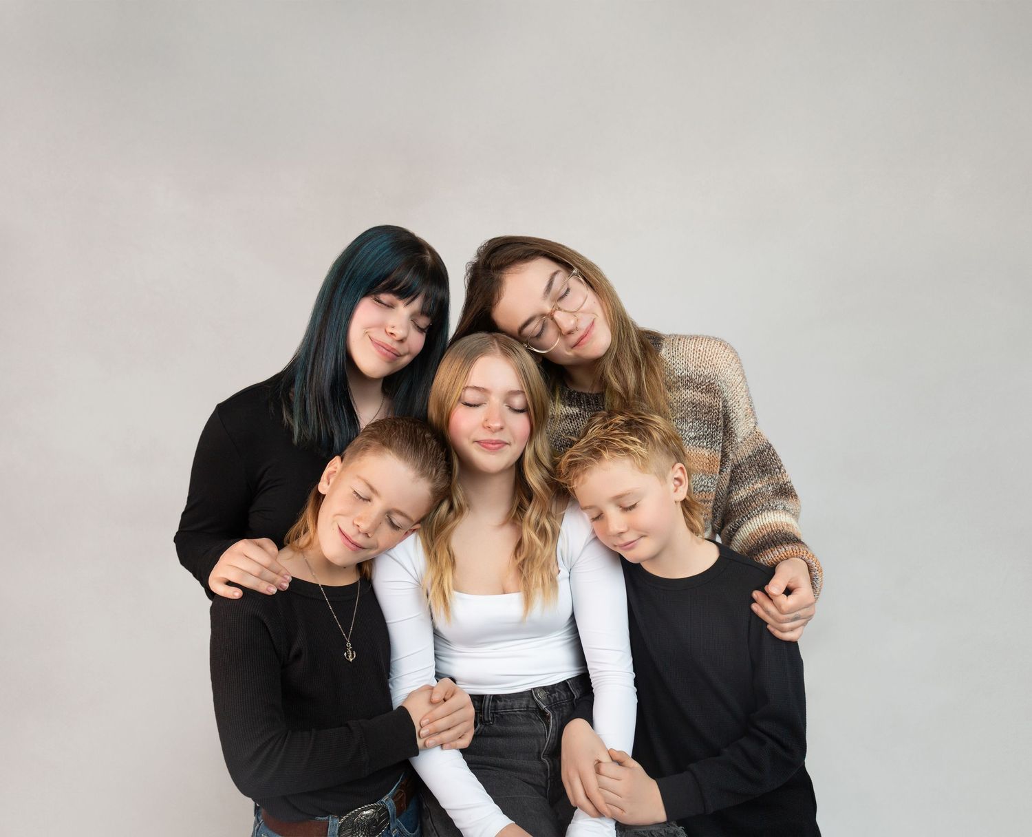 Five females of varying ages pose together in black outfits against a light gray studio background.