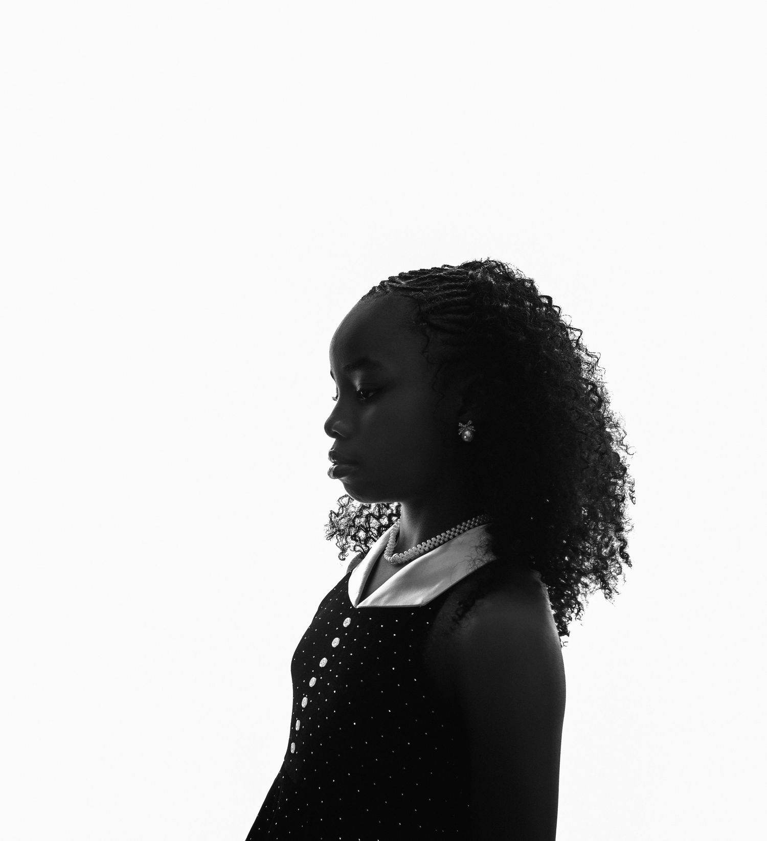Black and white profile portrait of a young woman with curly hair wearing a collared dress and necklace.