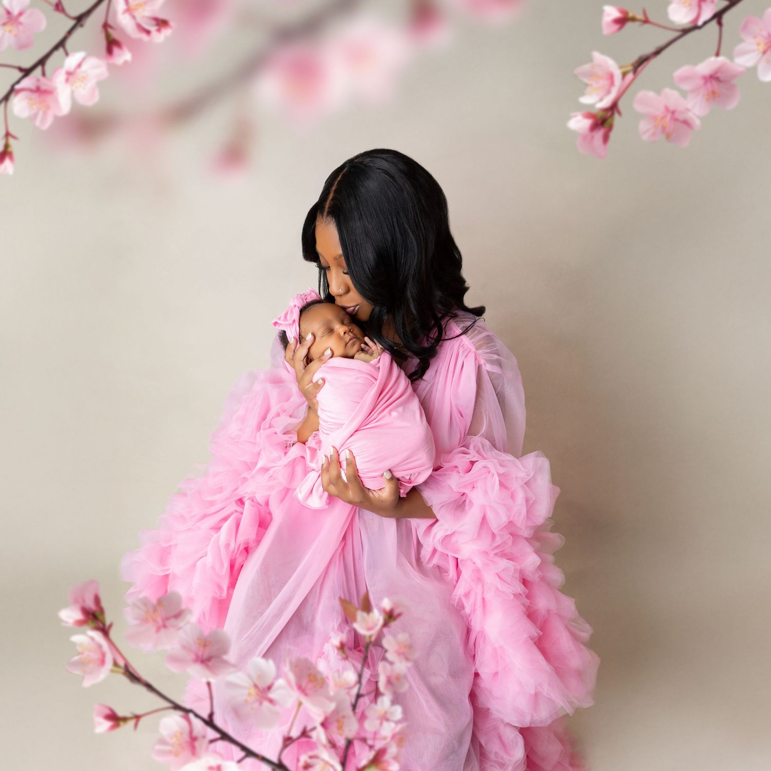 A mother in a pink ruffled gown tenderly holds her newborn baby, surrounded by blooming cherry blossom branches.