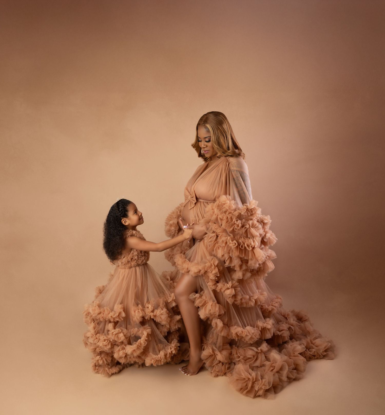 Pregnant woman and young daughter pose together in matching dusty rose ruffle tulle maternity gowns.