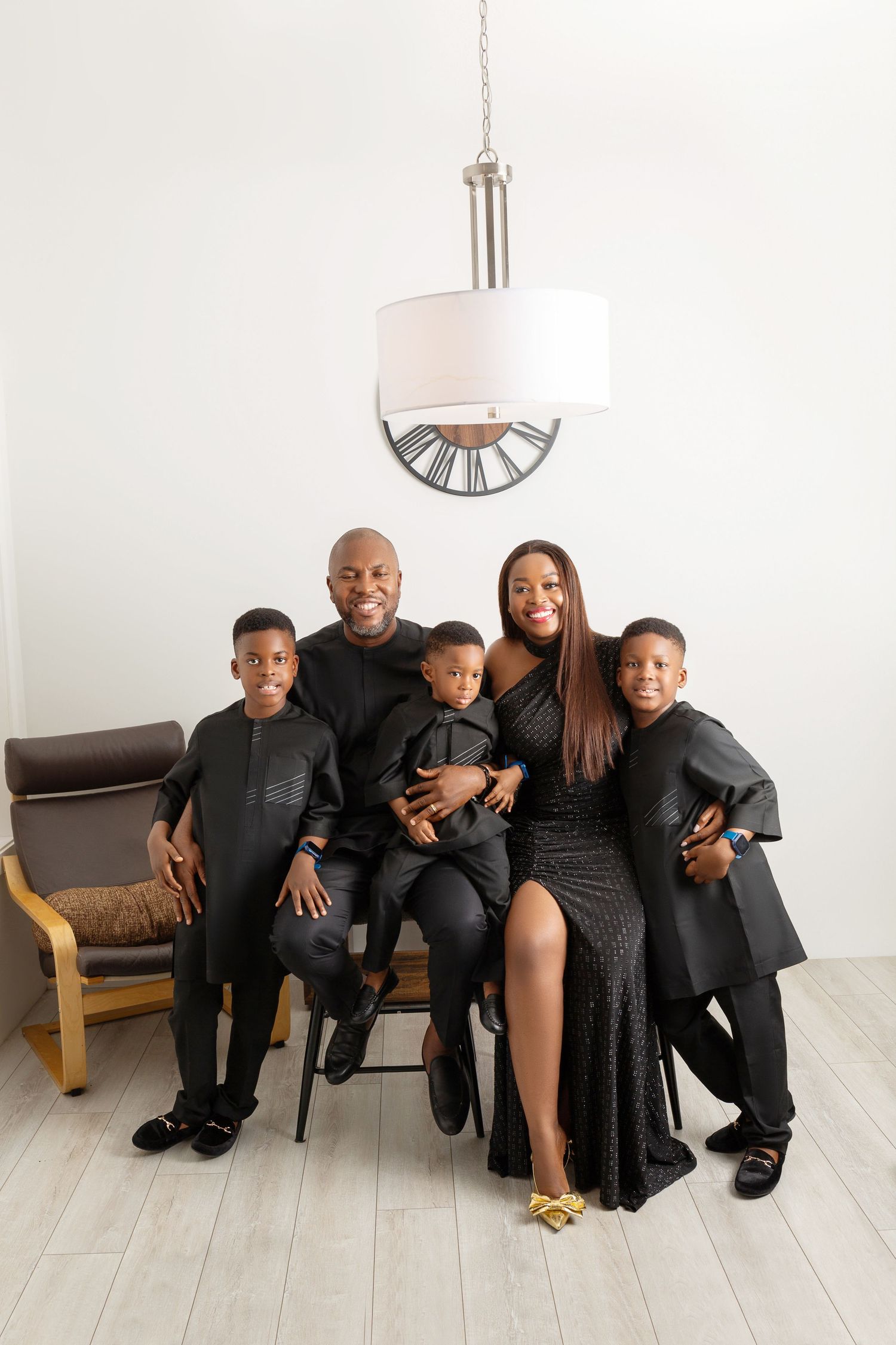 A joyful Black family of five poses together in matching black outfits against a bright white studio backdrop.