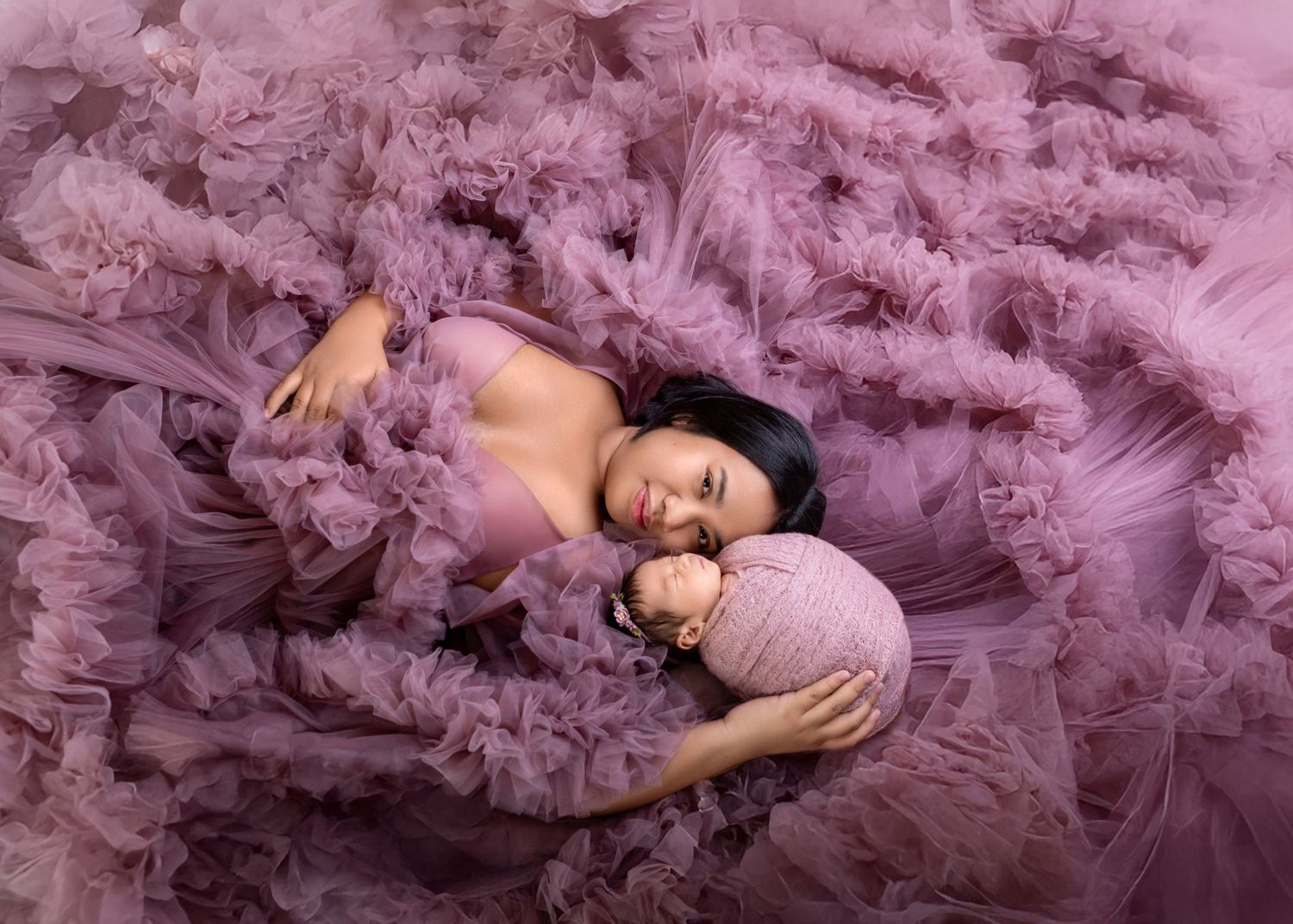 Overhead view of mom in purple tulle gown cradling swaddled newborn baby in studio portrait.
