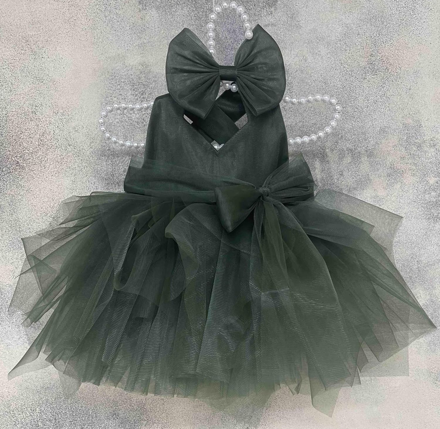 Dark green tulle girls dress with large bow displayed on a hanger for a formal occasion.