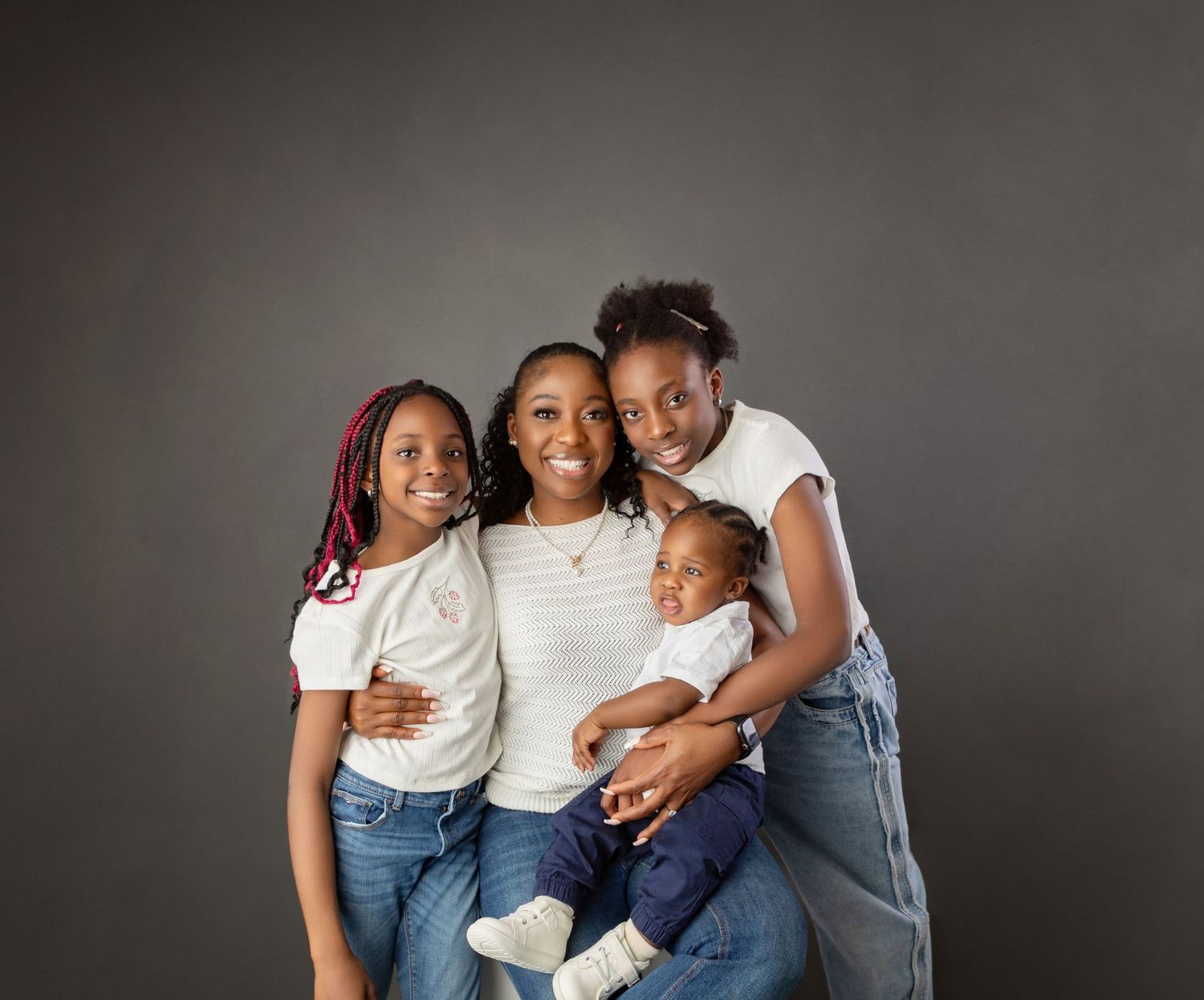 Mother with three children posing together in white tops and jeans in studio portrait.