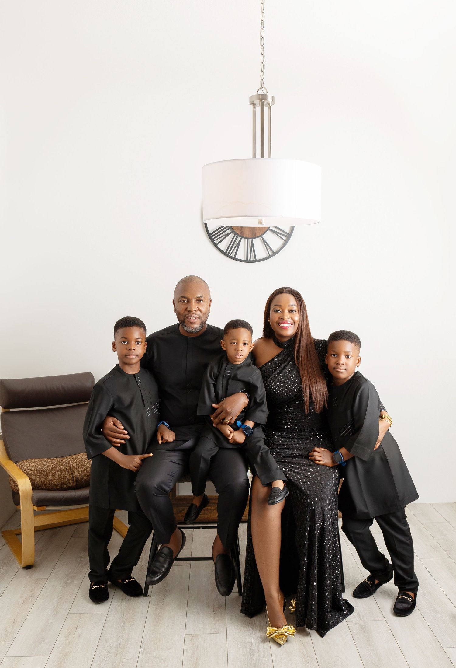 Family of five in matching black outfits posing together in bright white studio with chandelier.