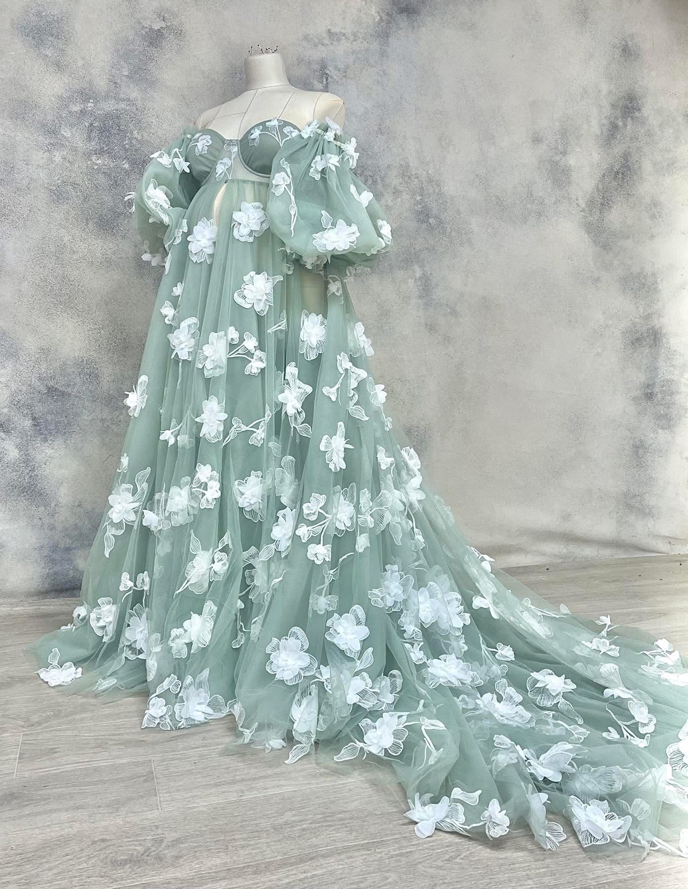Sage green off-shoulder tulle gown adorned with 3D white floral appliques and dramatic train.