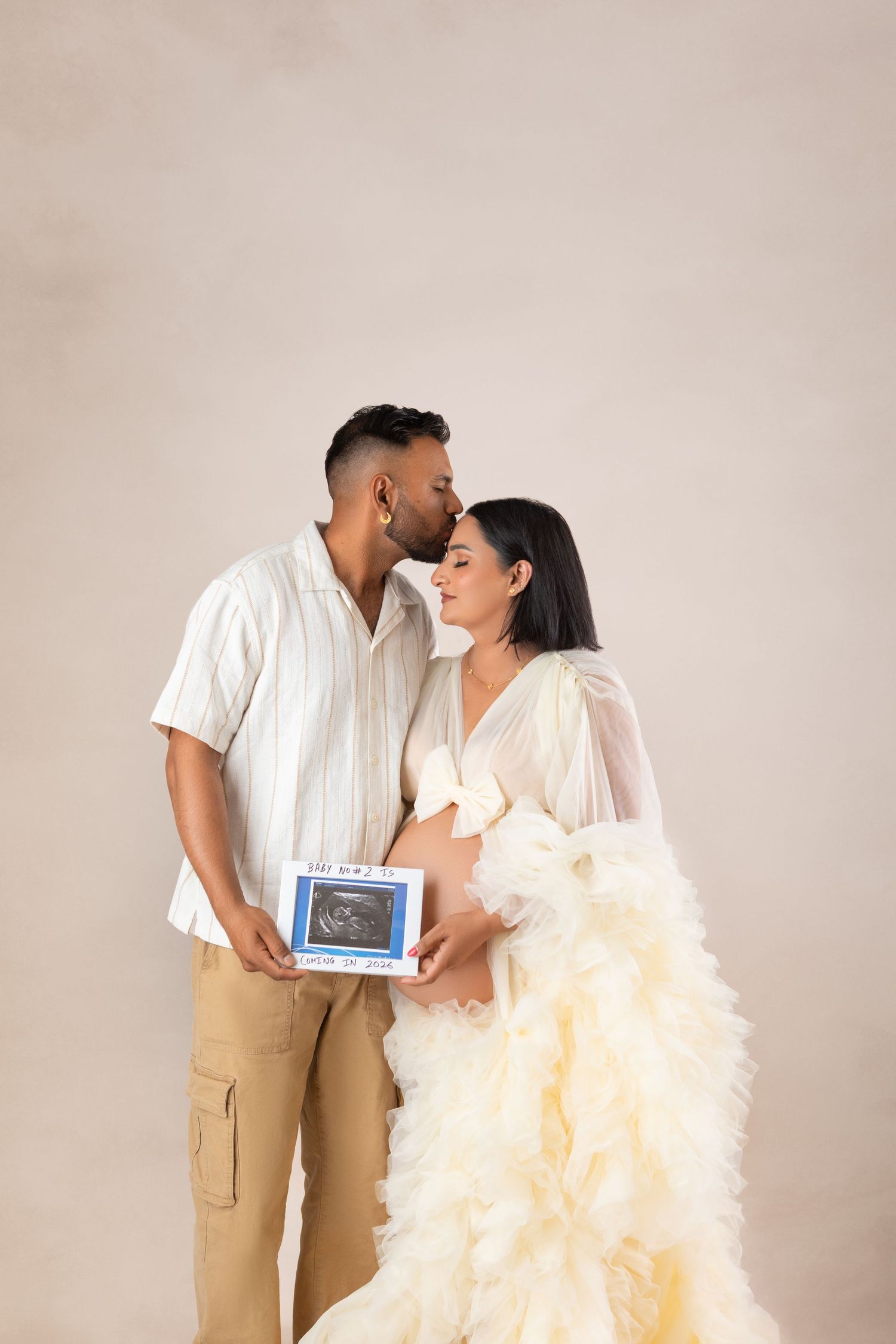 Couple sharing a tender kiss while holding an ultrasound photo, woman in elegant ruffled gown announcing pregnancy.
