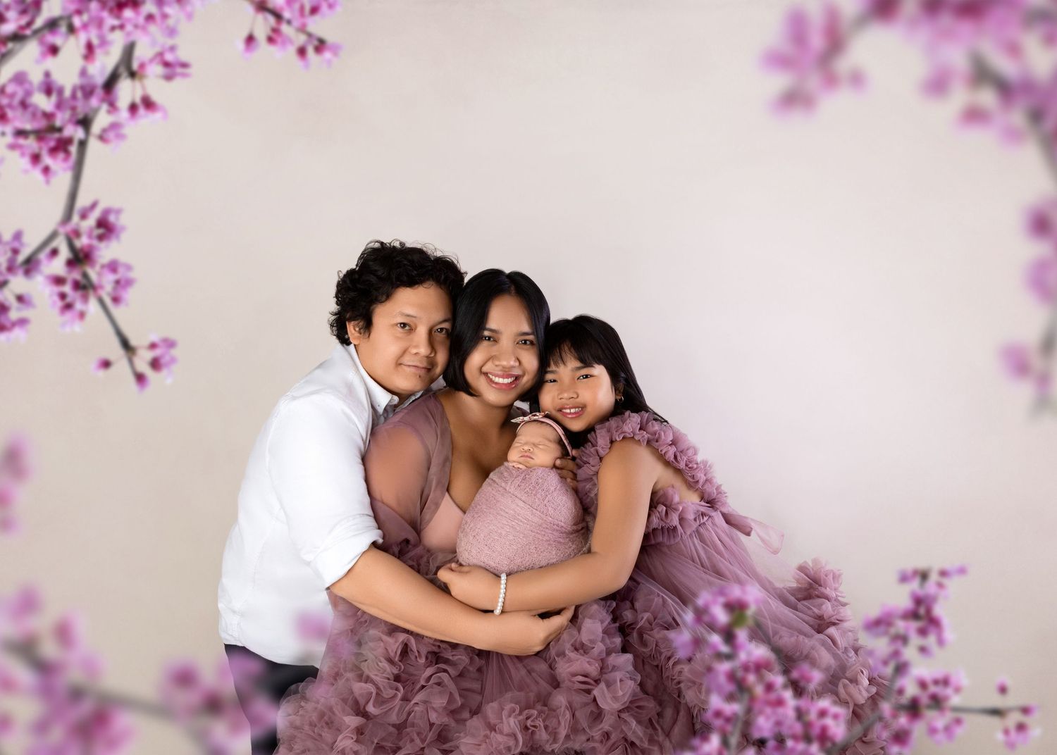 Family maternity photo with mom in purple tulle gown hugging two children among pink cherry blossoms.