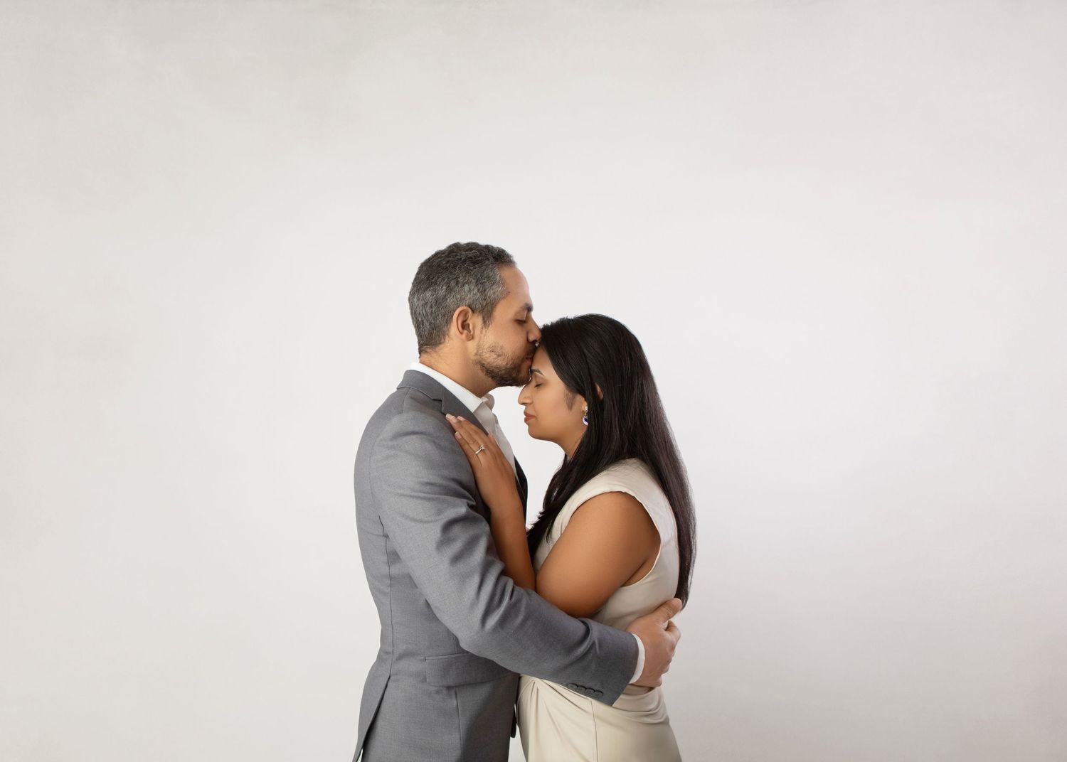 Romantic interracial couple embracing and touching foreheads tenderly against a white background.