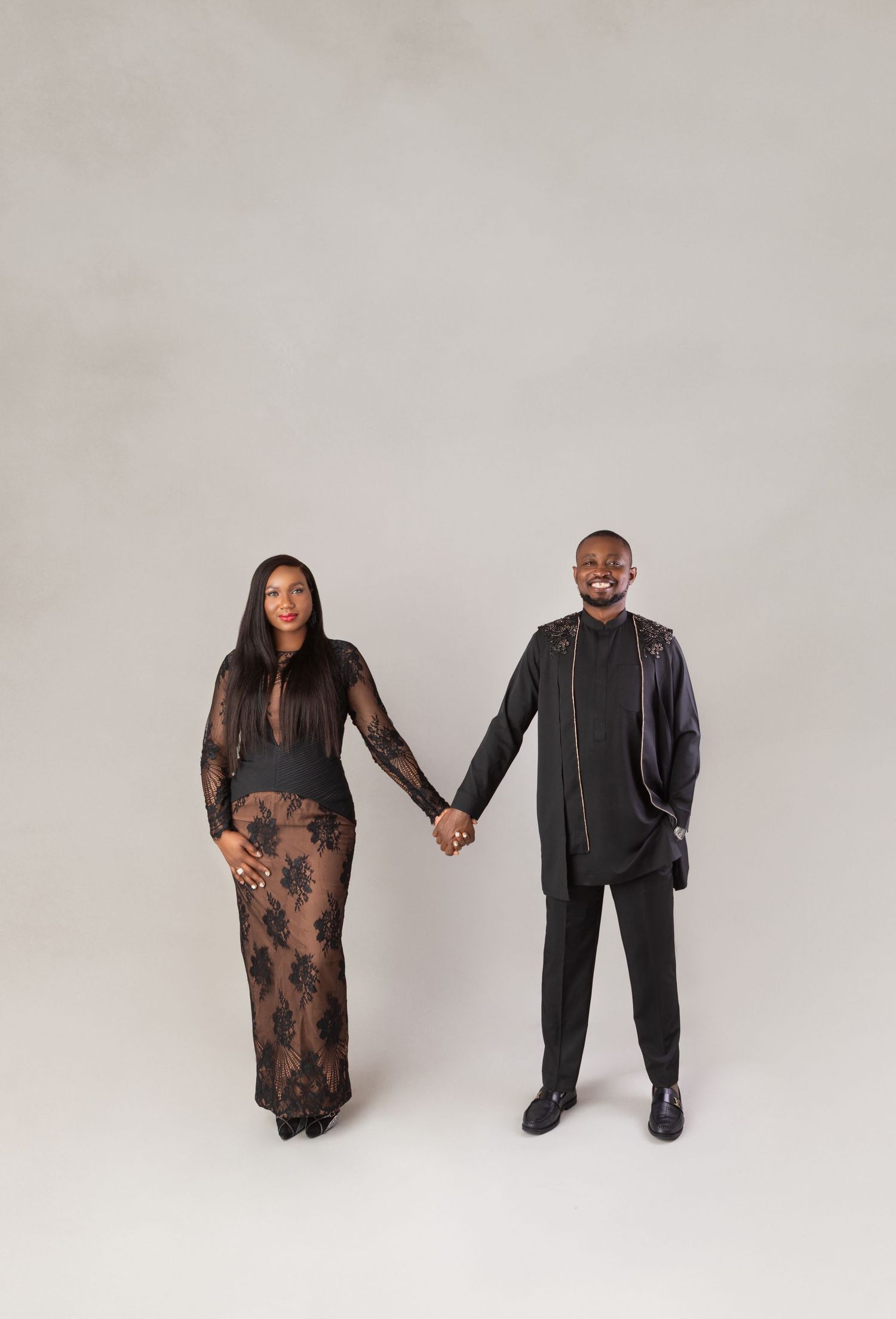 Elegant couple holding hands in matching black outfits during a studio portrait session.
