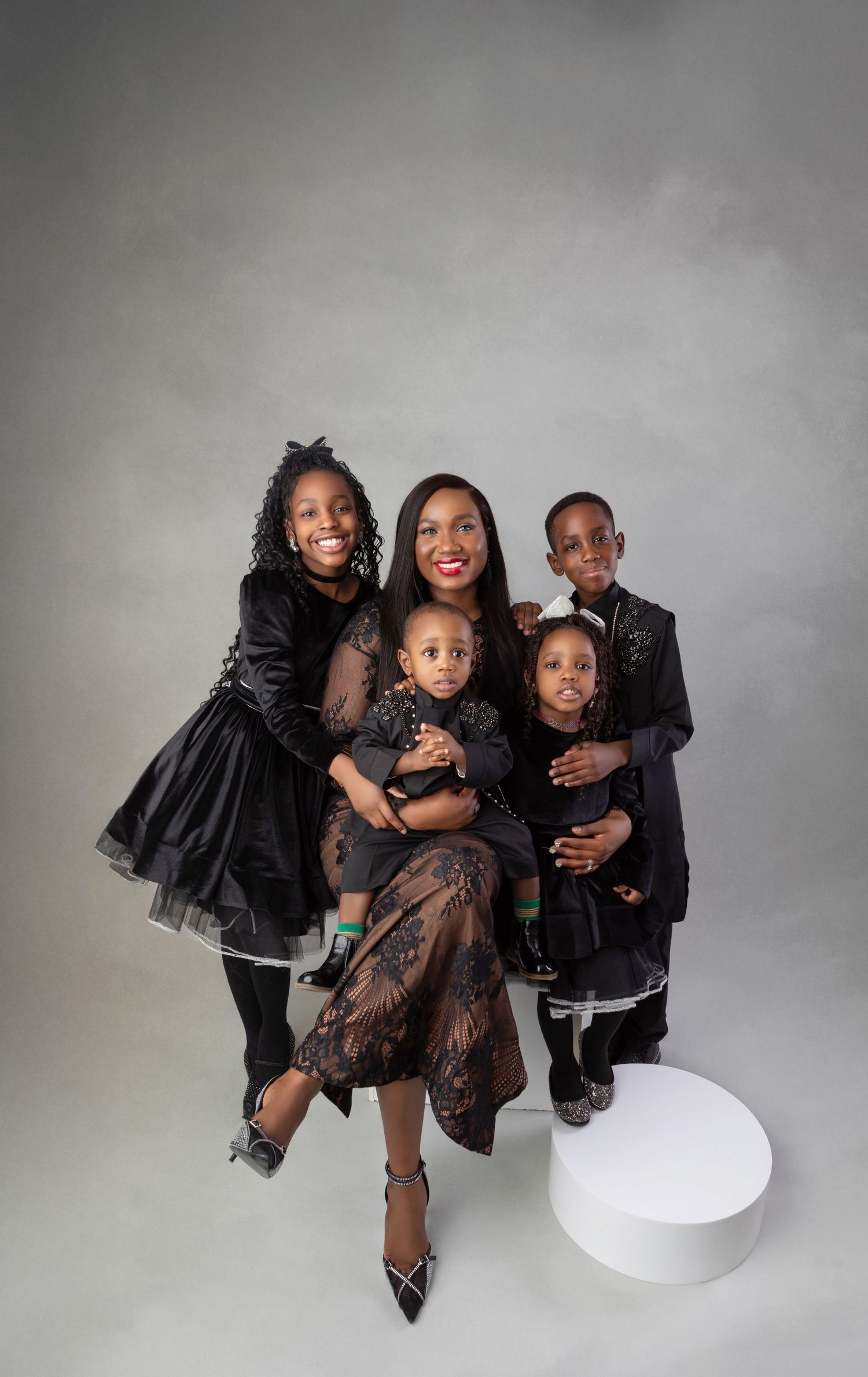 A joyful family of five dressed in elegant black outfits poses together for a professional studio portrait.