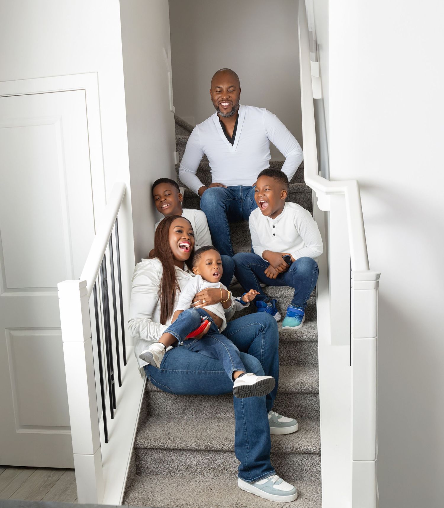 Joyful family of five laughing together on a carpeted staircase in a bright modern home.