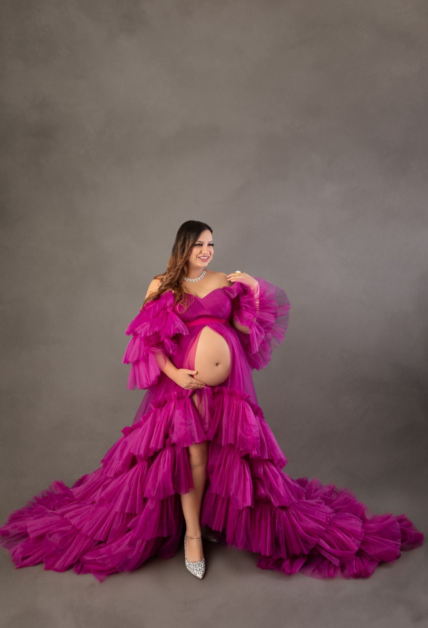Pregnant woman in vibrant magenta ruffled tulle maternity gown posing in professional studio portrait.