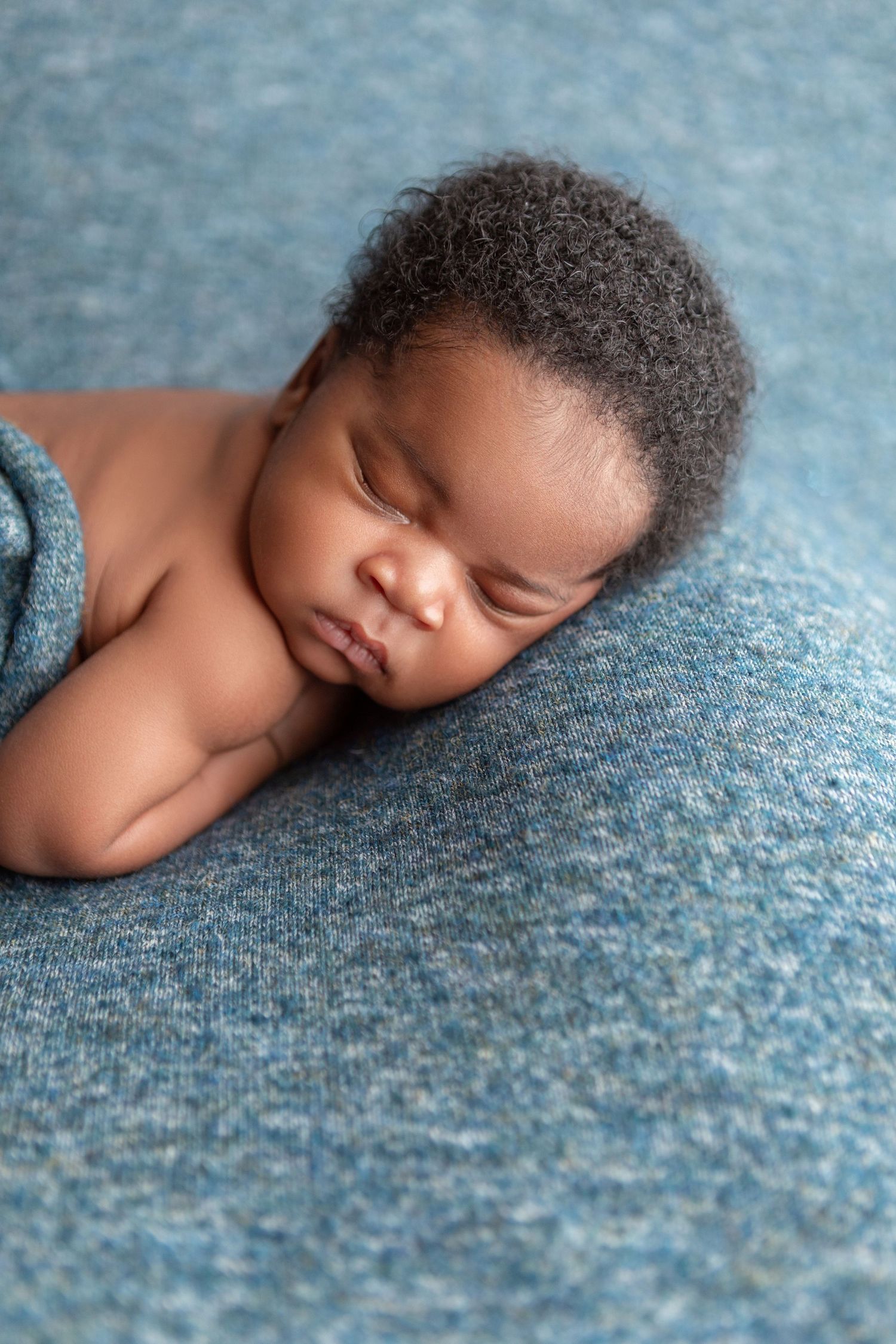 Peaceful newborn baby sleeping on a soft blue knit blanket in a cozy newborn photography portrait.