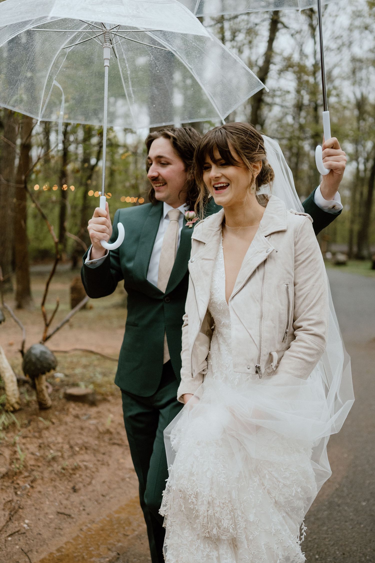 Couple laughing while holding clear umbrellas on rainy wedding day.