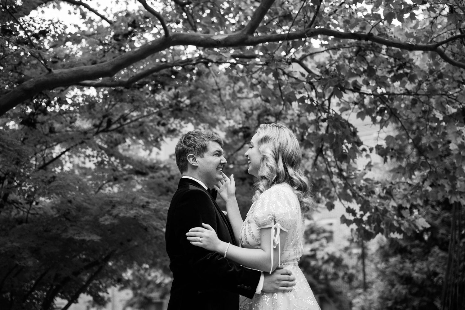 A romantic moment captured between newlyweds under a tree canopy in black and white.