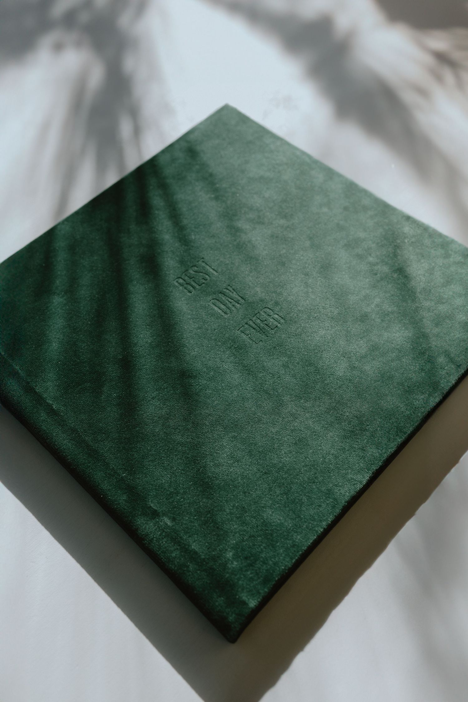 A green velvet photo album cover with embossed details on white fabric background.