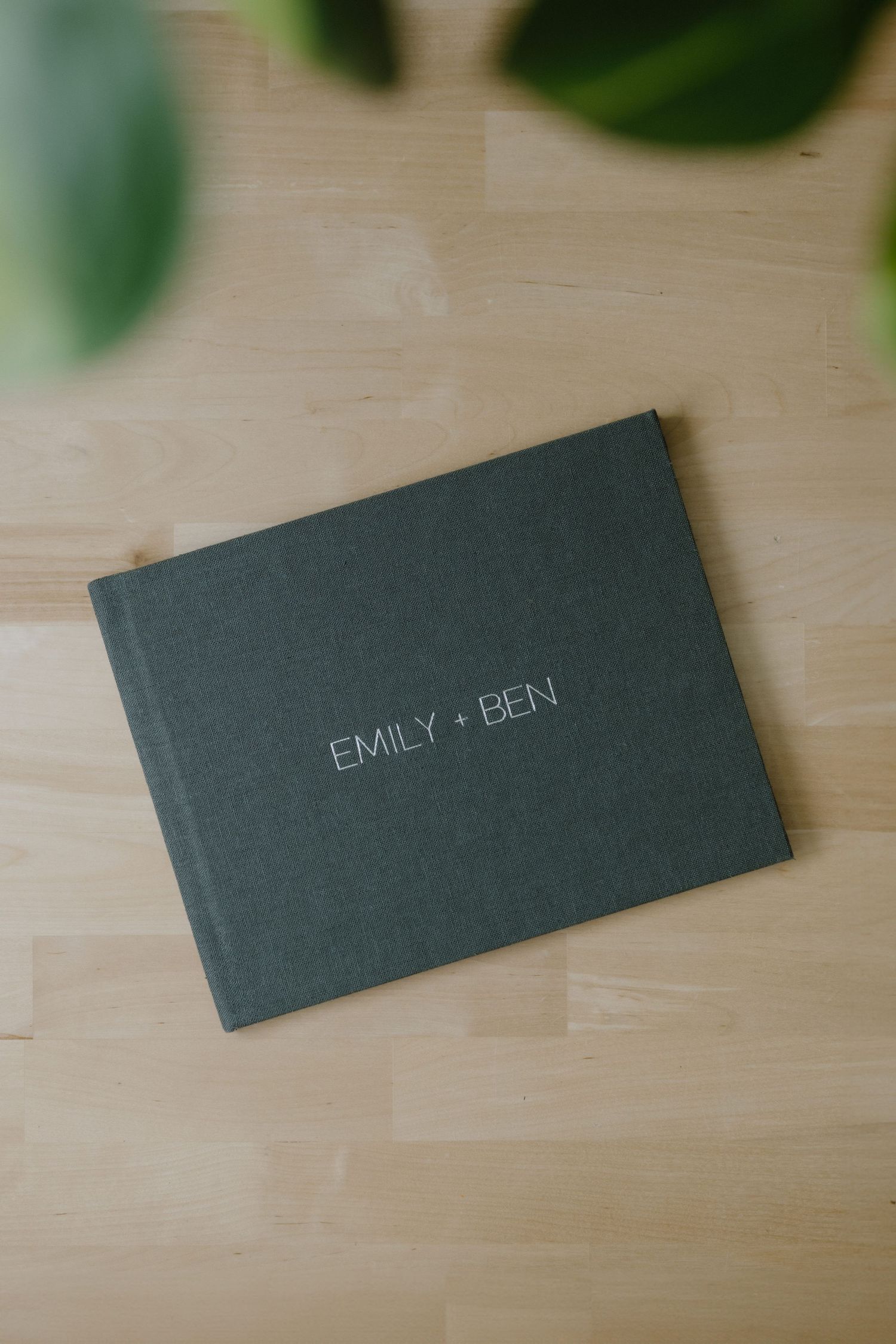A grey hardcover photo album with names in silver text on a wooden surface.