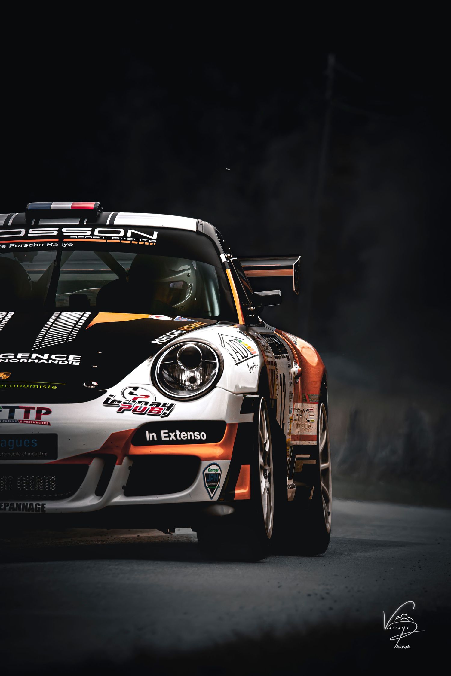 Three white Porsche race cars with orange and black racing liveries showcased in dramatic low-key lighting.