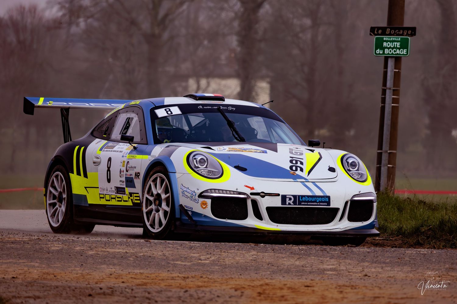 White racing car with neon yellow accents parked on a track during an overcast day.