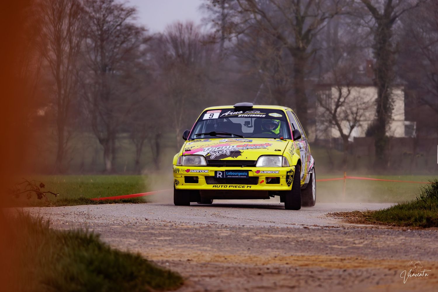 Yellow and blue rally car speeds through a winding forest road during an autumn competition.