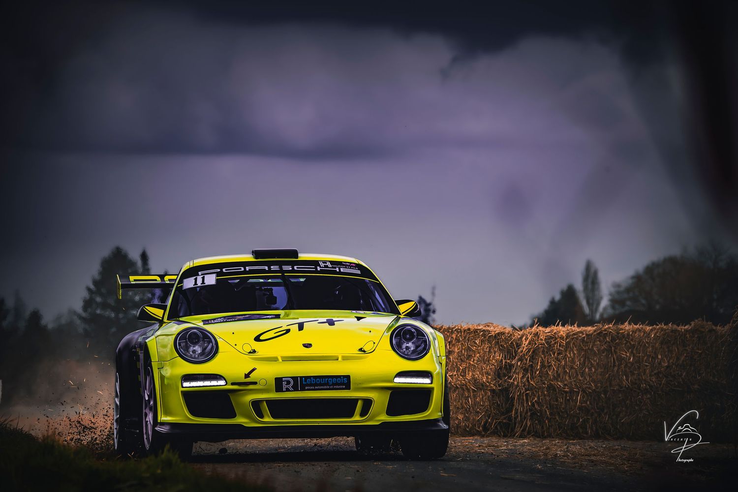 Bright yellow Porsche race cars lined up against a moody sunset backdrop with autumn foliage.