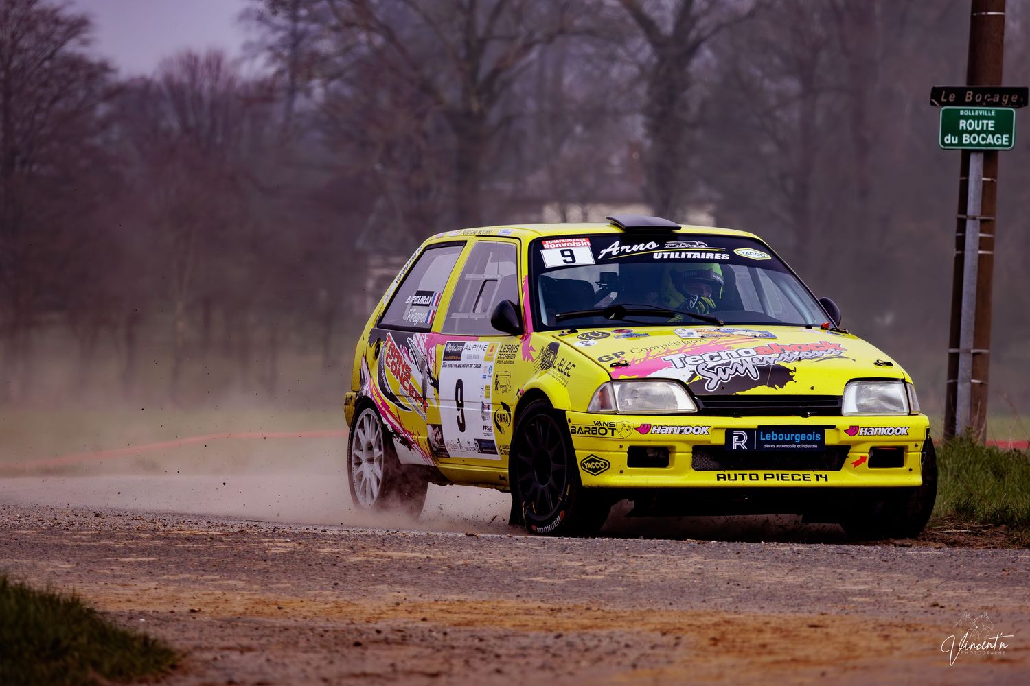 Yellow rally car kicks up dust while racing on a dirt track during a competitive motorsport event.