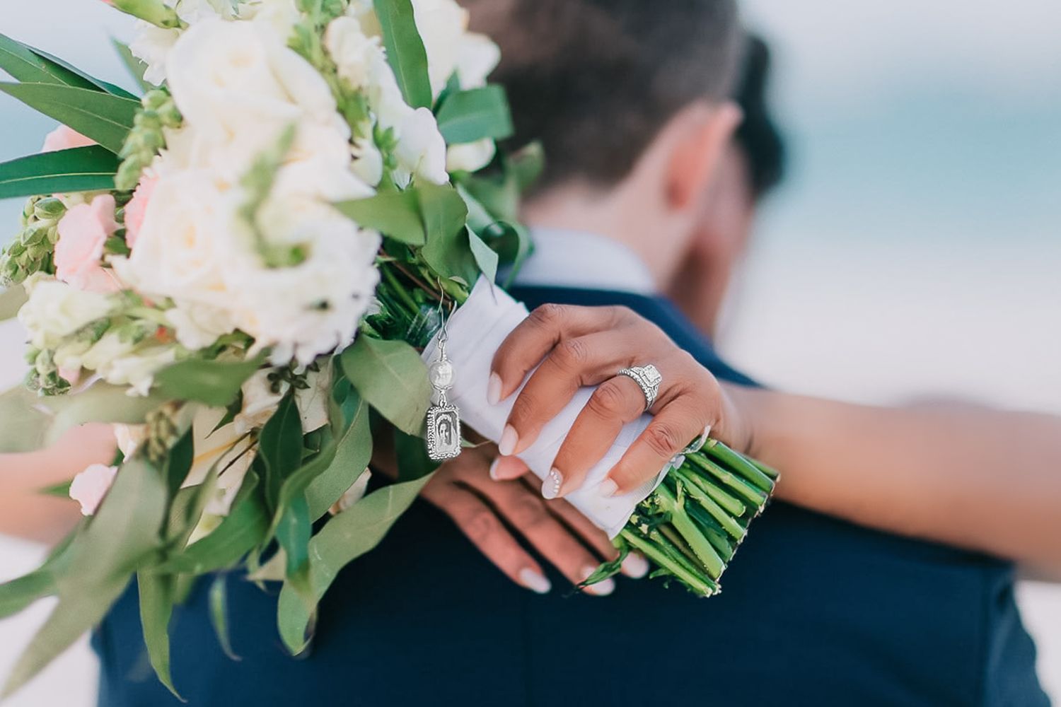 Close up of hands holding an elegant white wedding bouquet with green foliage wrapped in white ribbon.
