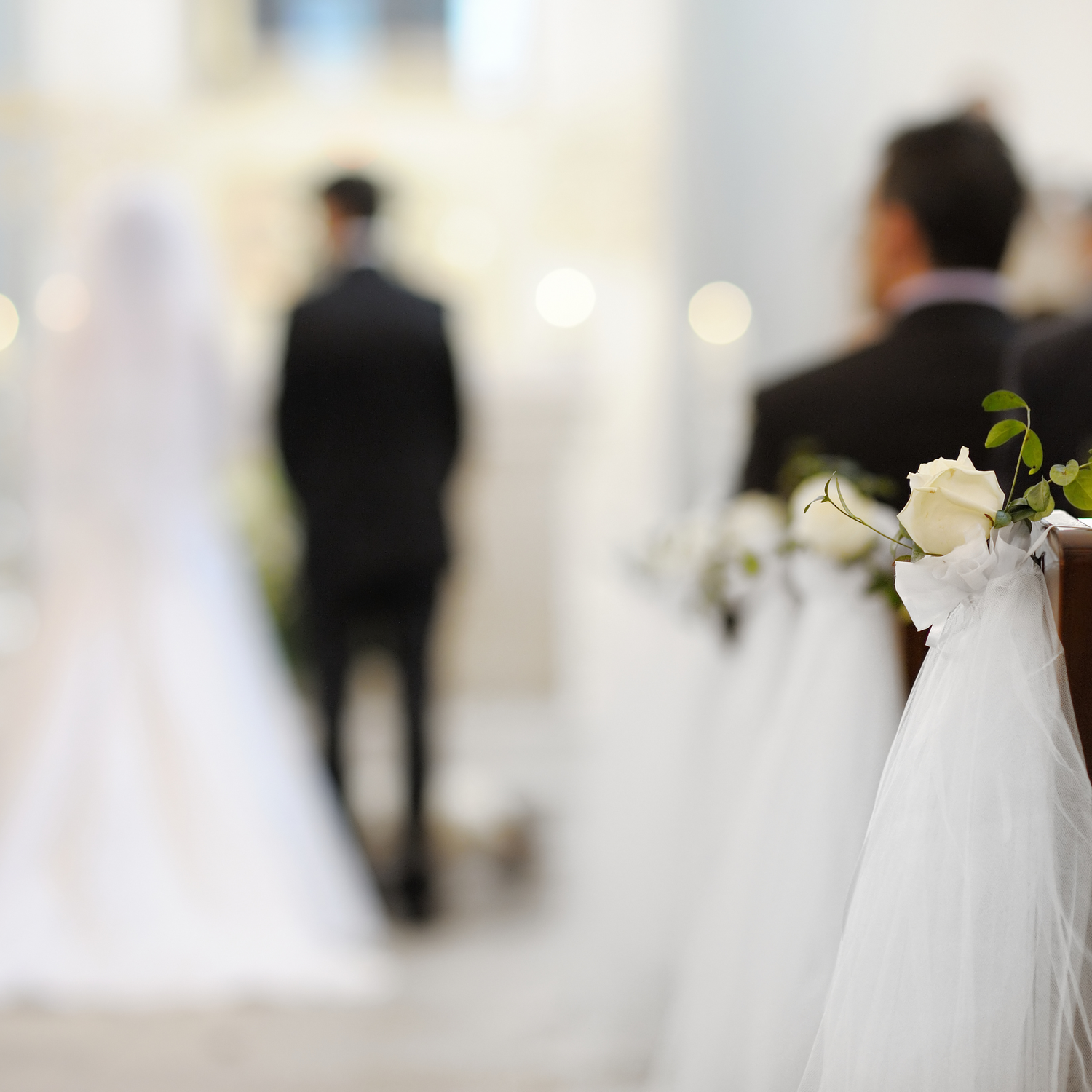 Soft focus view of wedding ceremony venue with white bridal veils and flowers in foreground as someone walks away.
