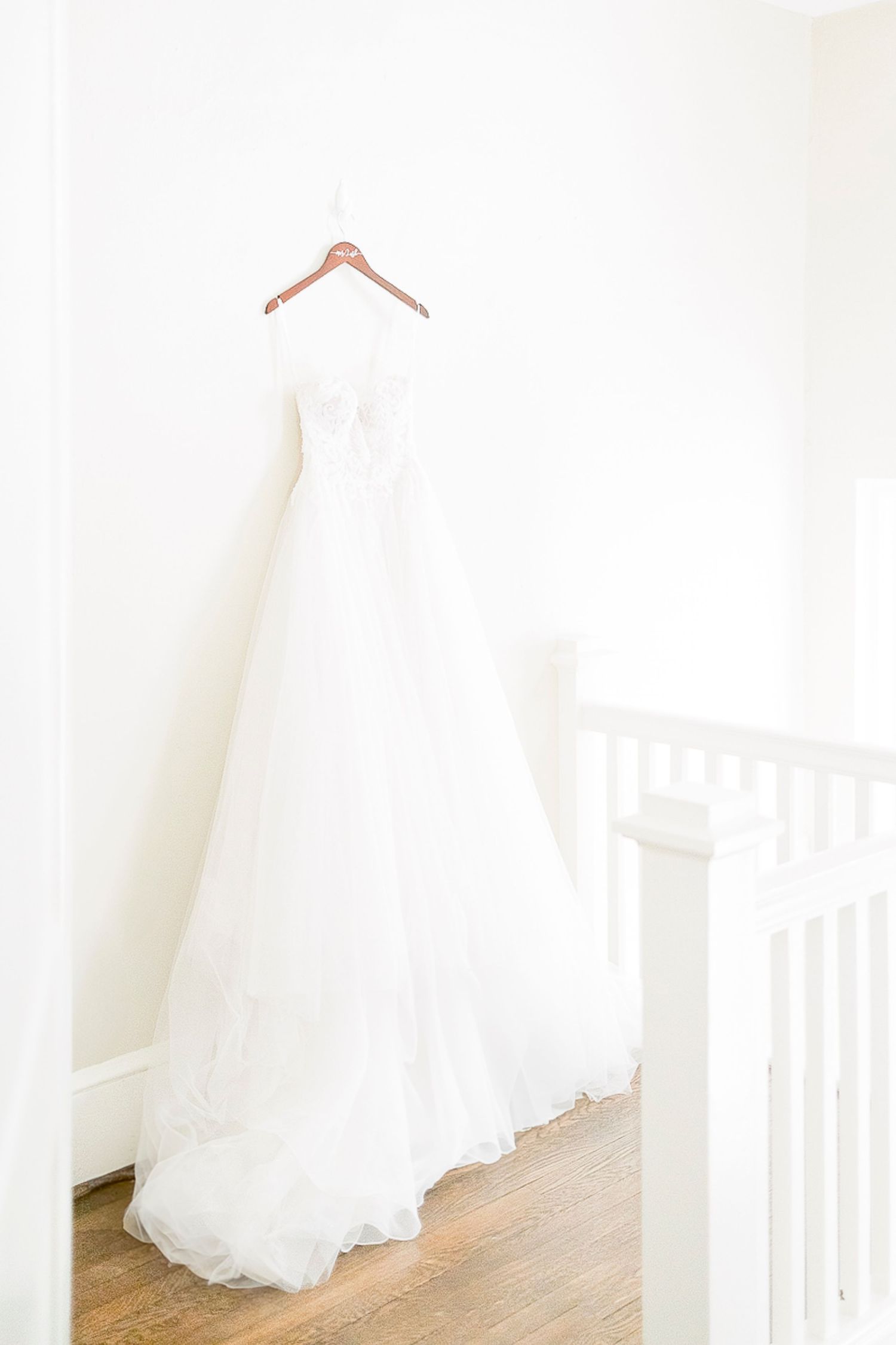 Three elegant white wedding dresses hanging on wooden hangers against a light-colored wall.