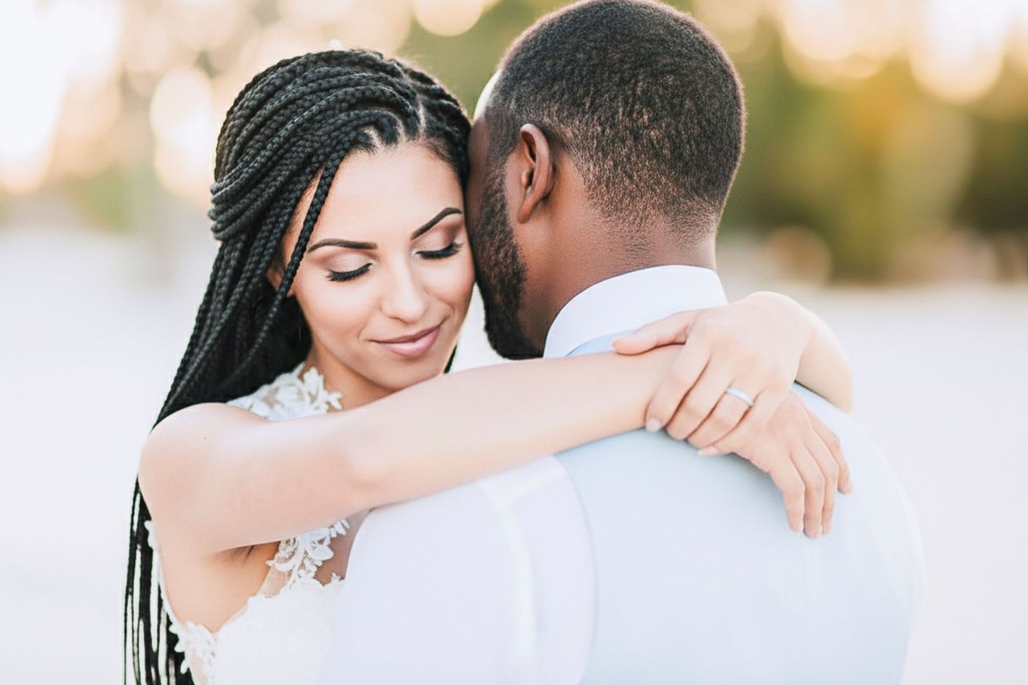 Romantic couple embraces during outdoor photoshoot with soft golden sunset lighting in the background.
