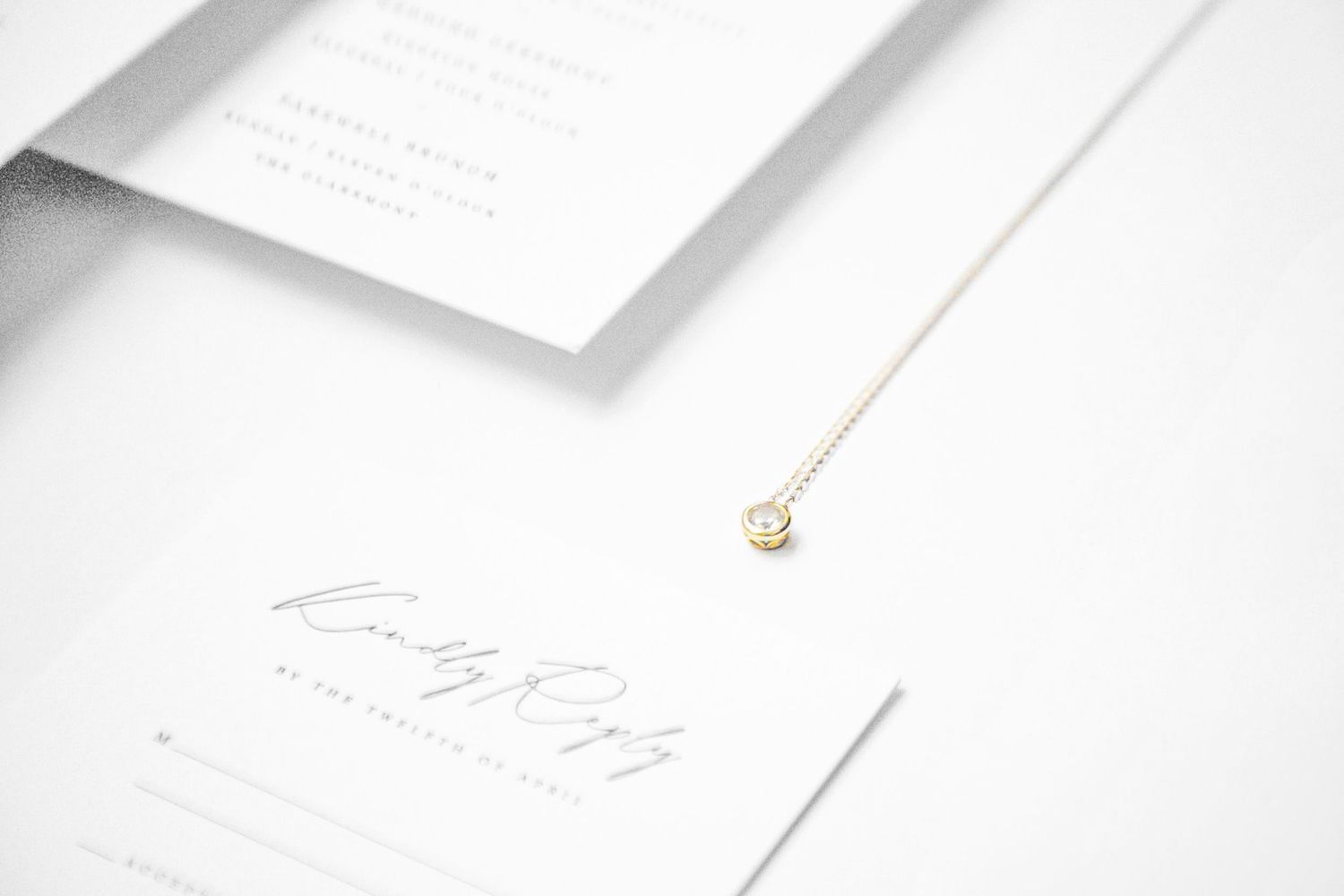 Elegant white wedding stationery suite with a delicate gold necklace pendant on a minimalist white background.