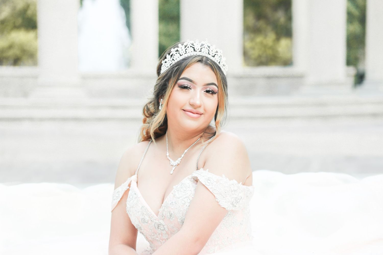 A bride in a white lace wedding dress and floral crown poses outdoors with a joyful expression.