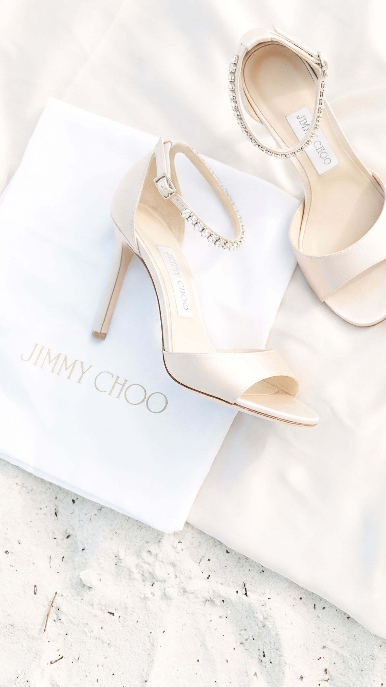 Elegant Jimmy Choo nude satin heels with crystal ankle strap displayed on white dust bag.