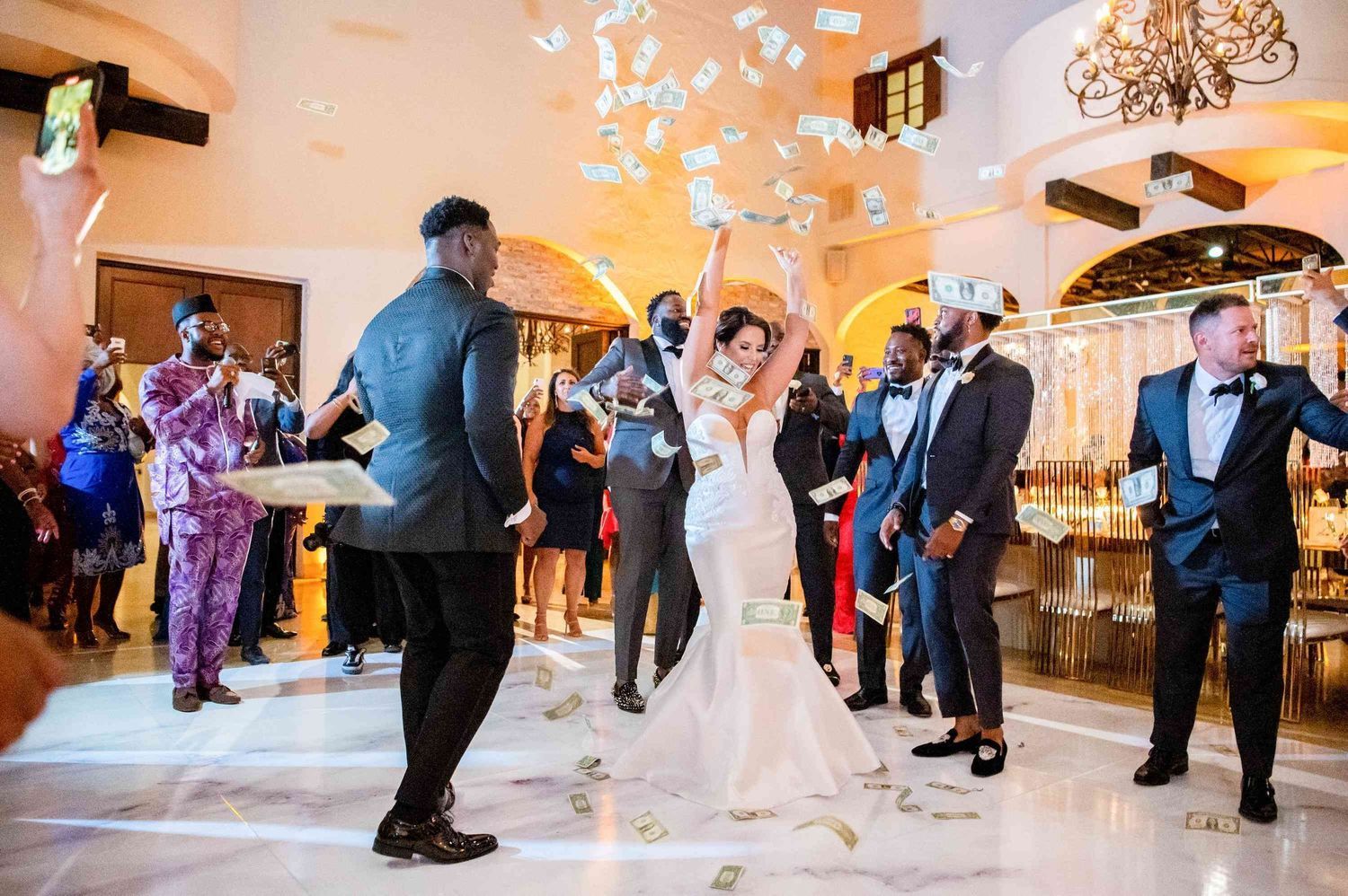 Wedding guests dancing together on an elegant ballroom floor illuminated by warm lighting and crystal chandeliers.