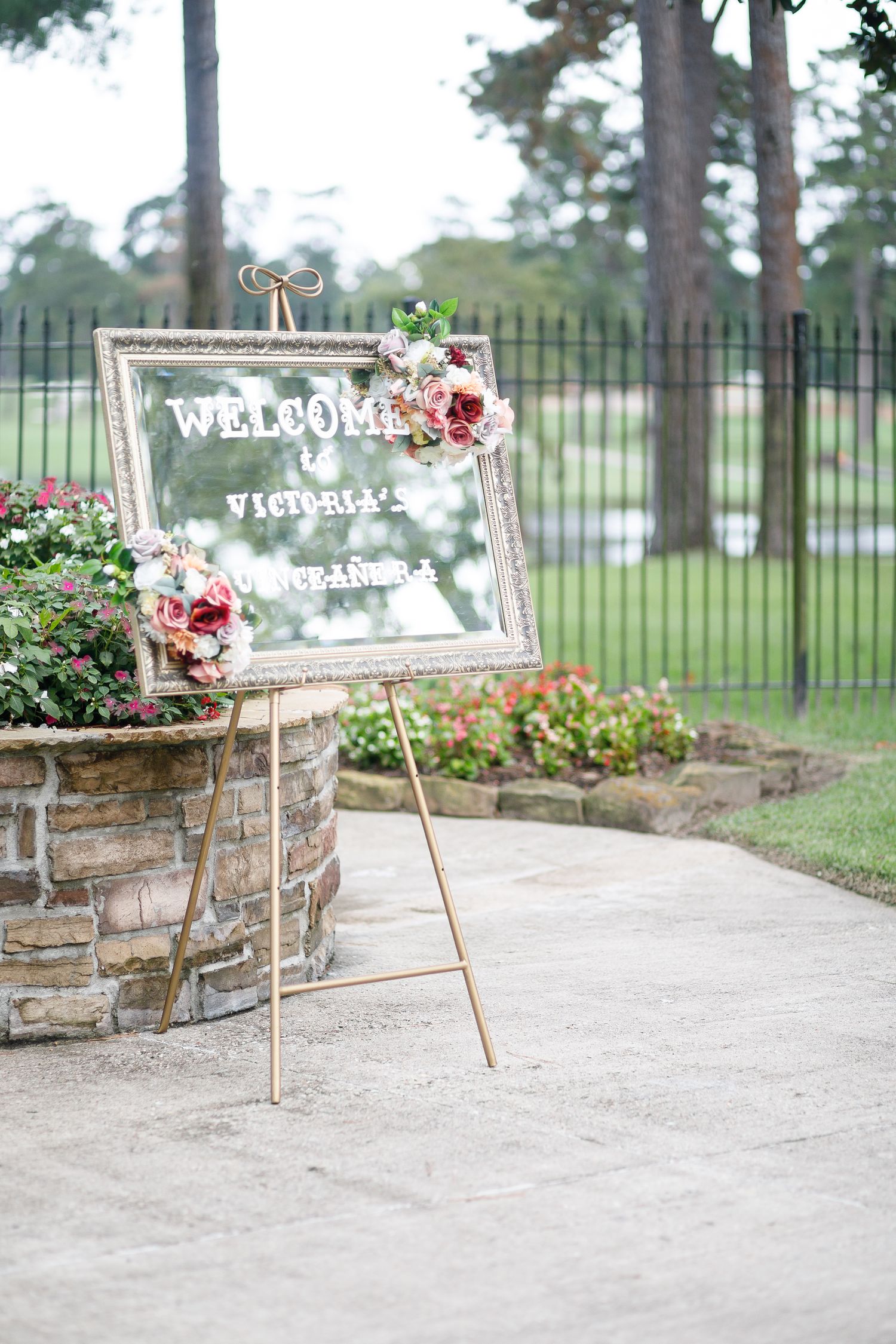 Vintage white welcome signs with floral decorations stand along a stone-lined garden path at an outdoor venue.