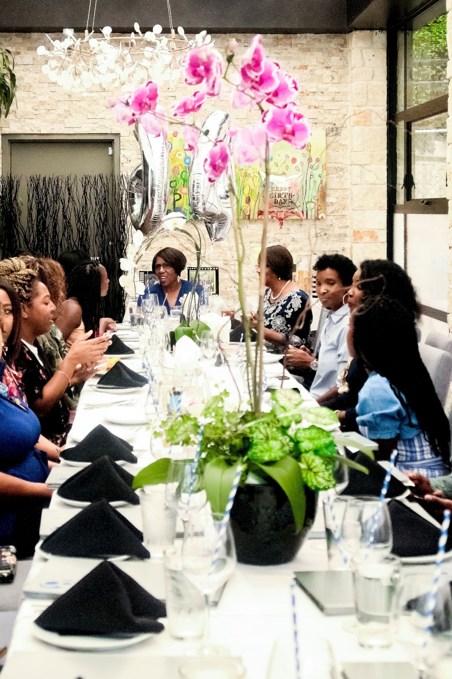 Women gathered around elegant dining table with pink orchid centerpiece and silver balloons at a celebratory luncheon.