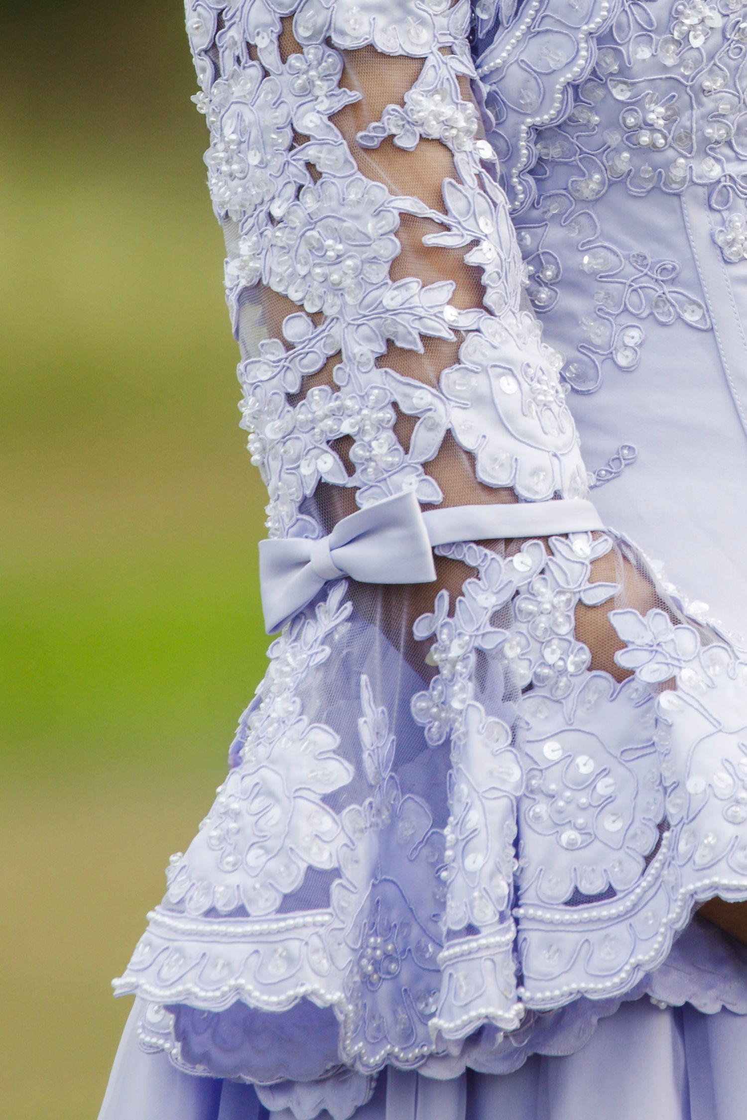 Close-up details of delicate white lace trim and ruffles on a light lavender dress or gown.