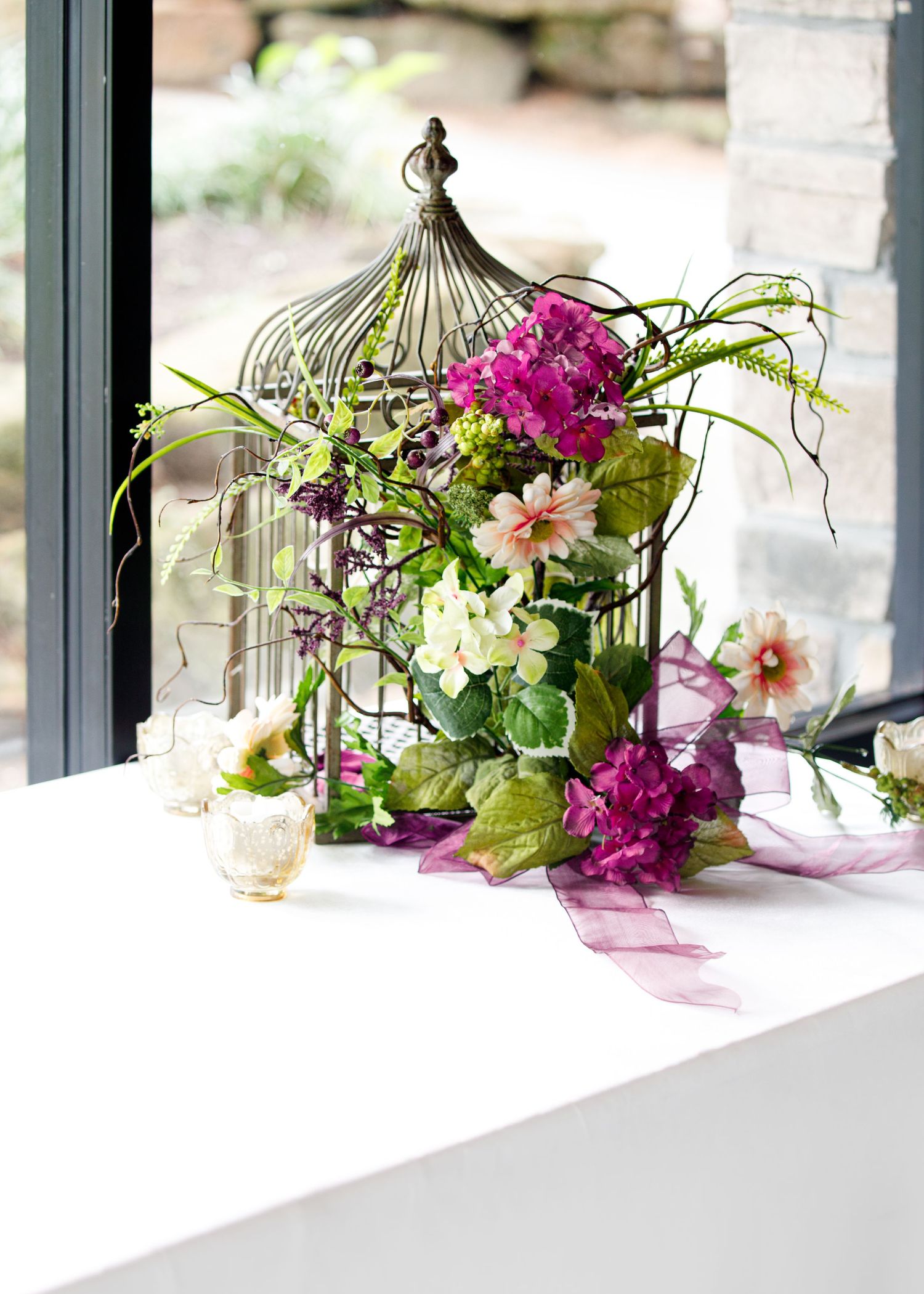 Decorative birdcages with floral arrangements and purple orchids create an elegant display on white windowsills.