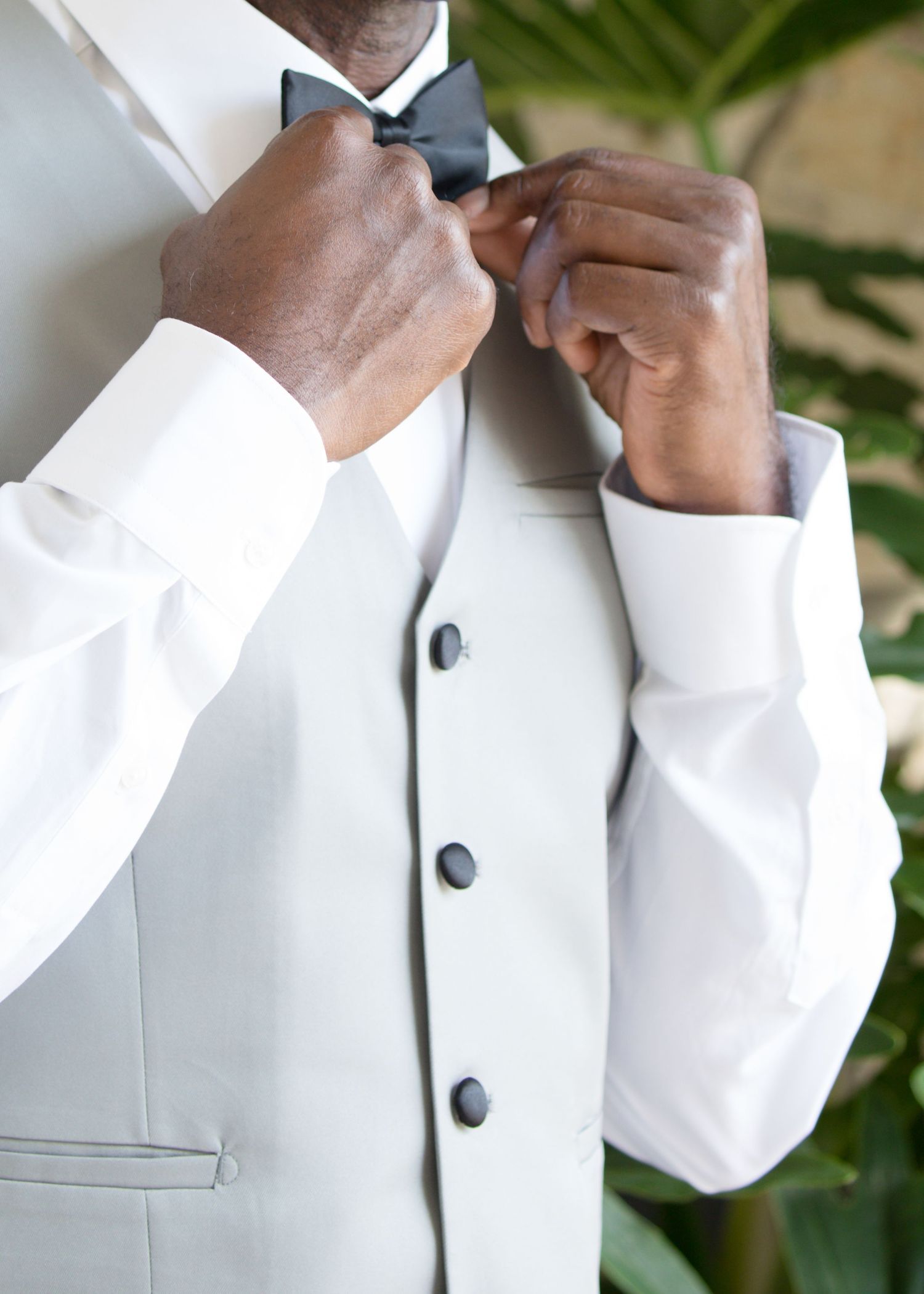 A close-up view of someone adjusting a white bowtie on a formal tuxedo collar.