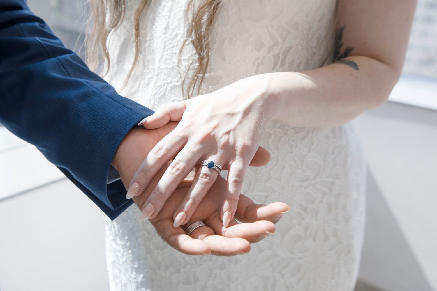 Bride and groom holding hands showing sapphire engagement ring and wedding bands at ceremony.