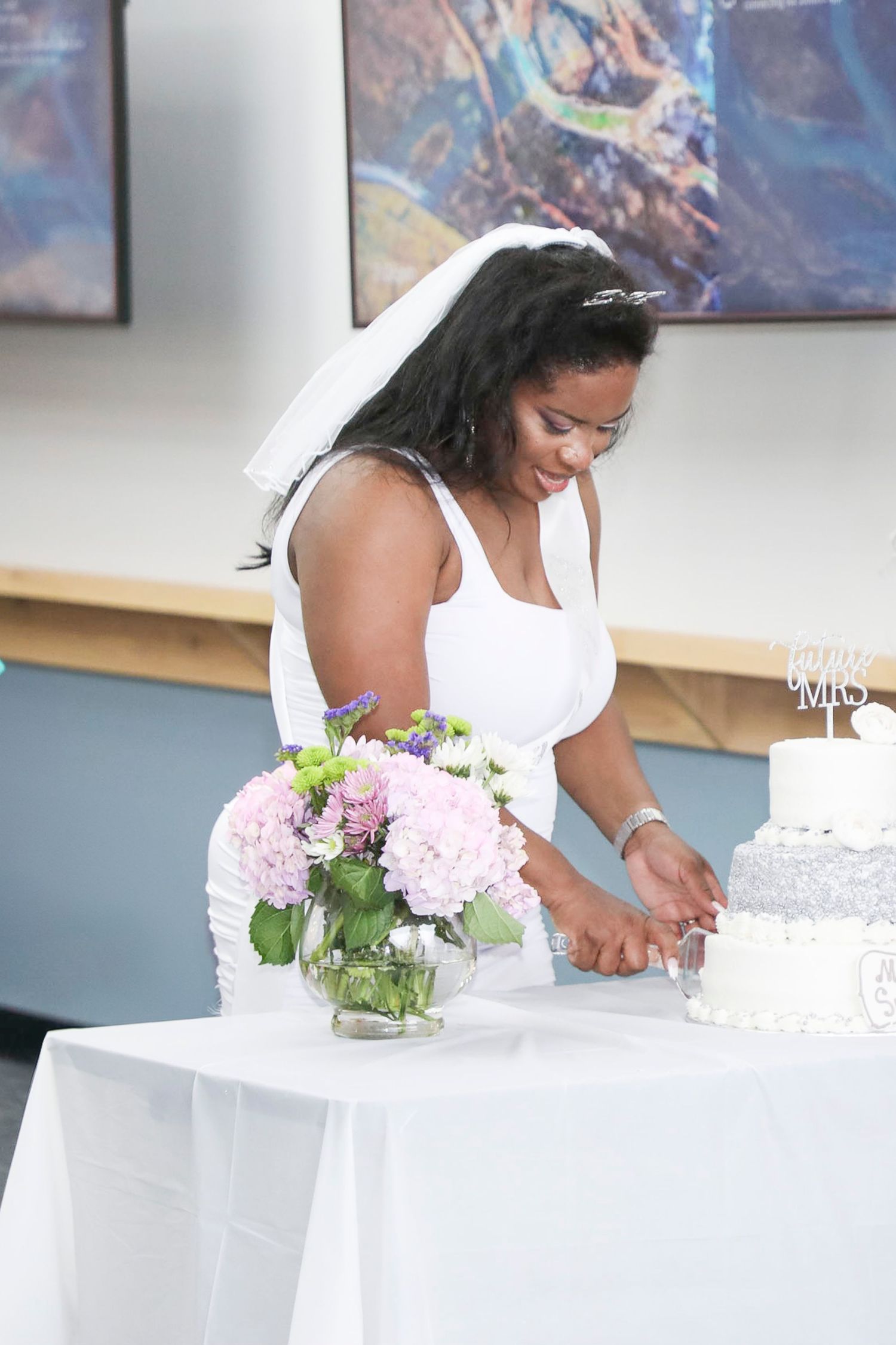 Event decorator arranges delicate pink hydrangeas in glass vases on white tablecloths during wedding setup.