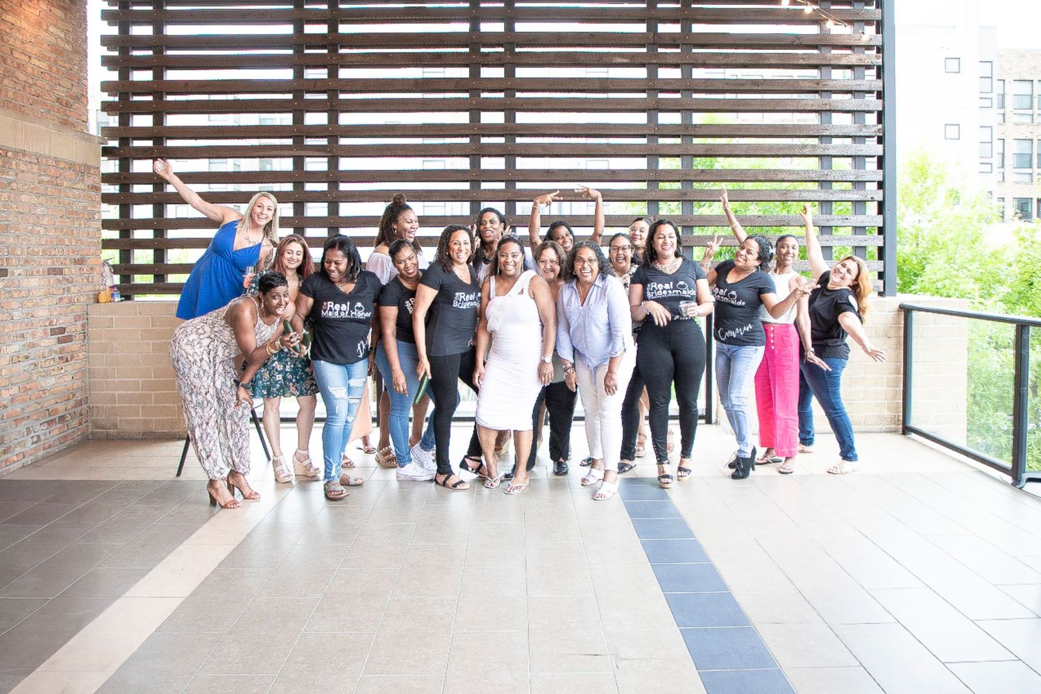 A large group of people posing together on a modern building terrace with wooden slat walls and glass railings.