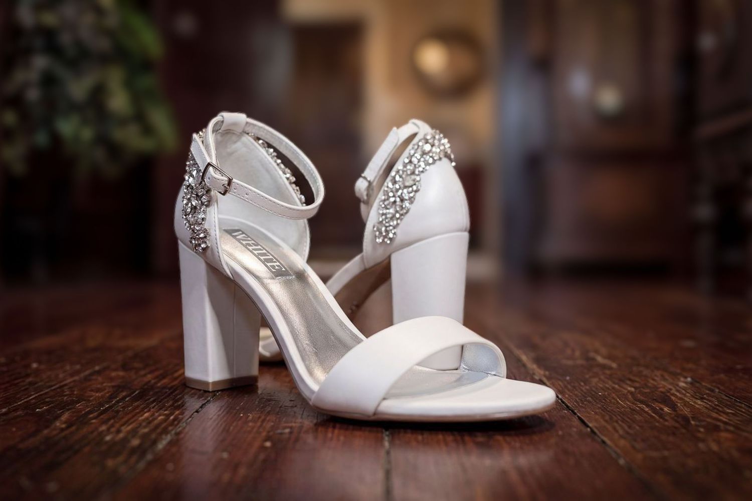 White block heel bridal sandals with crystal embellishments displayed on a wooden floor.