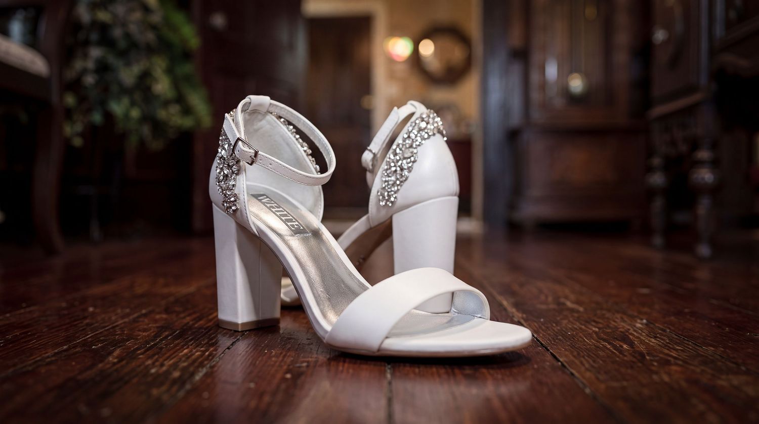 Elegant white bridal block heel sandals with crystal embellishments on ankle strap displayed on hardwood floor.